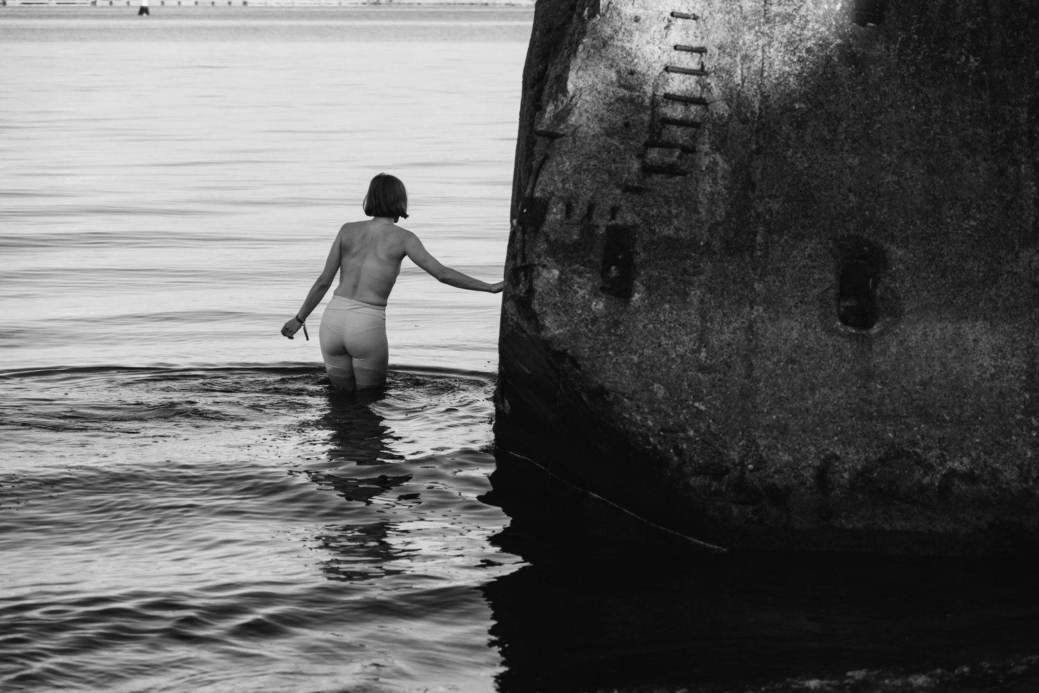 Swimmers explore around large concrete structures in dark water.