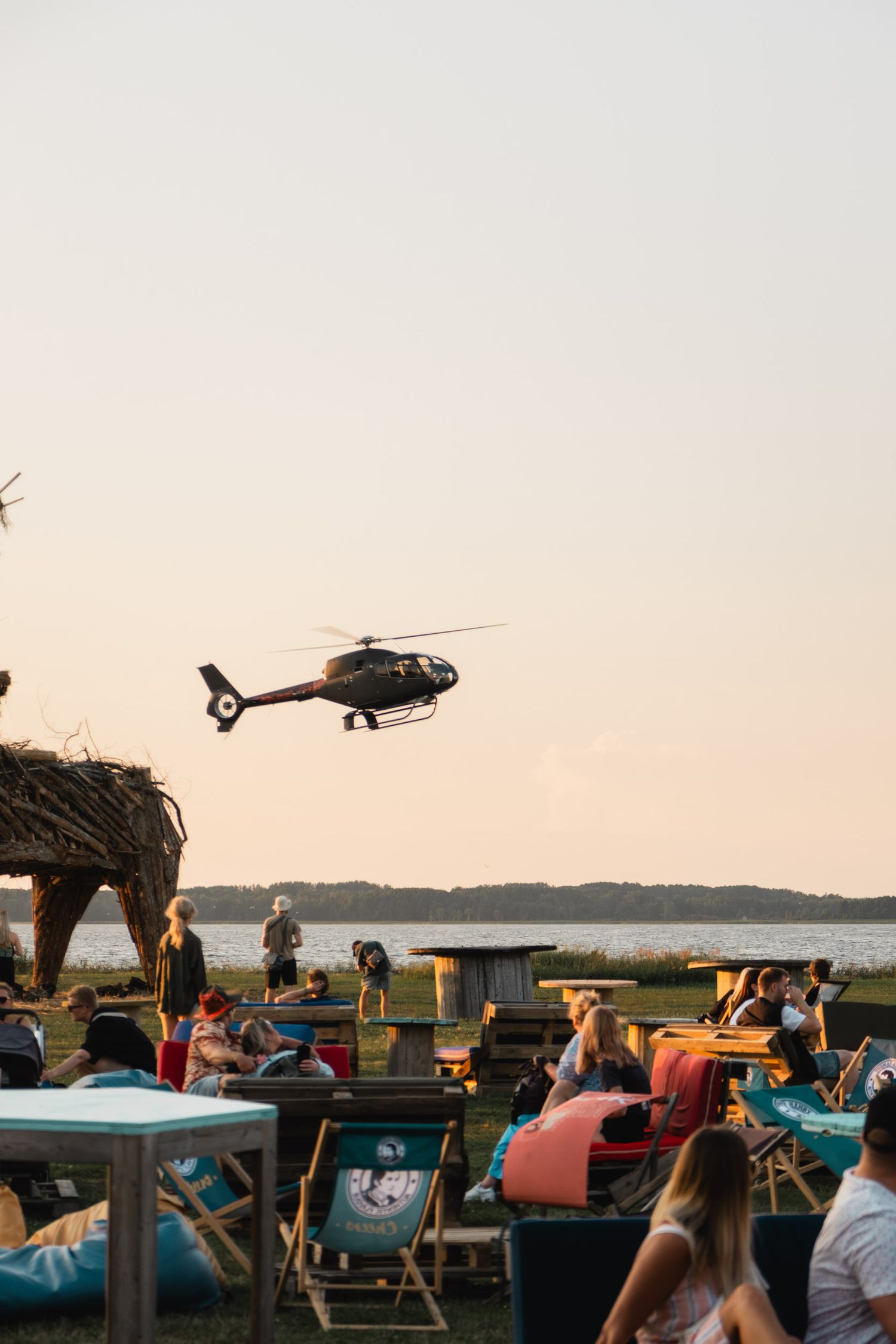 Crowd of festival attendees watching a helicopter fly overhead during sunset.
