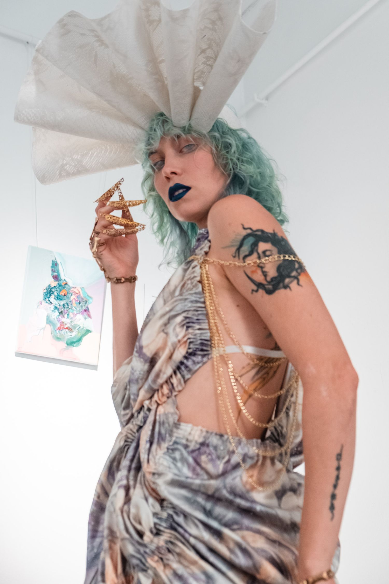 Alternative fashion look with teal hair, fan headpiece, and tattoos in muted tones.