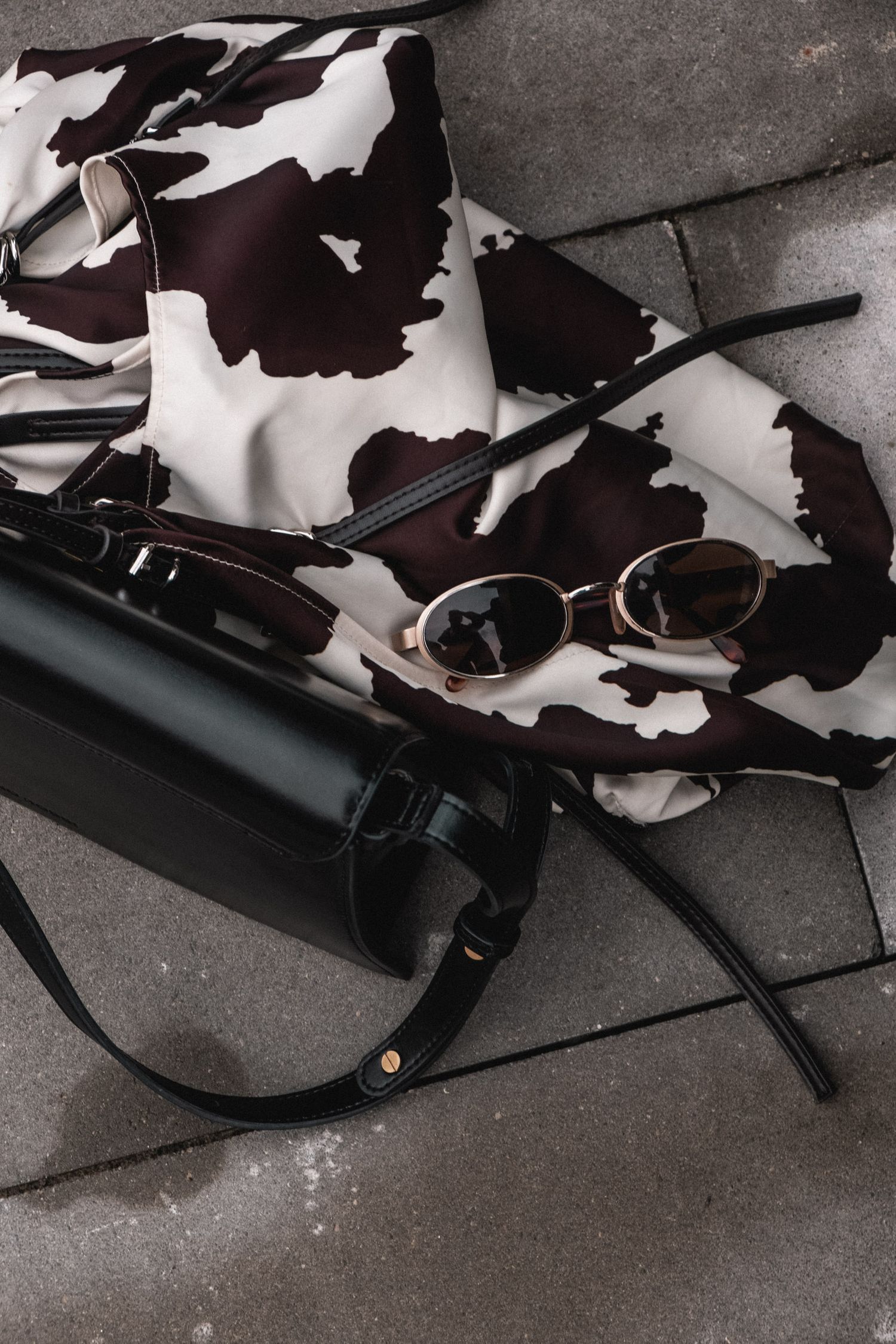 Black and white cow print pattern with sunglasses and camera equipment on concrete surface.