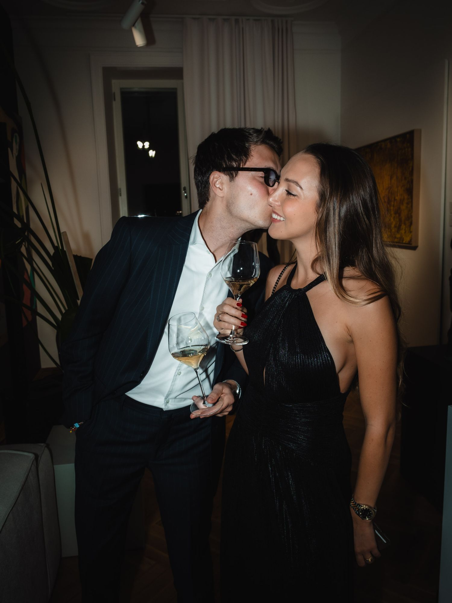 A couple shares an intimate moment while enjoying wine glasses in a dimly lit room.