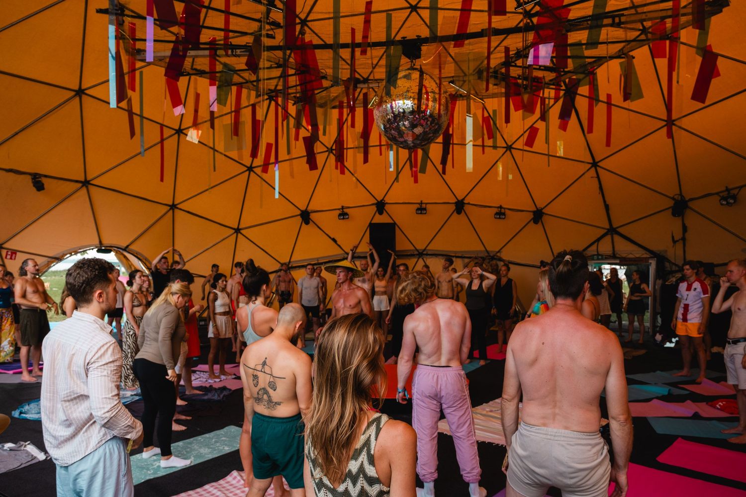 Large group of people dancing under tent structure at outdoor festival.