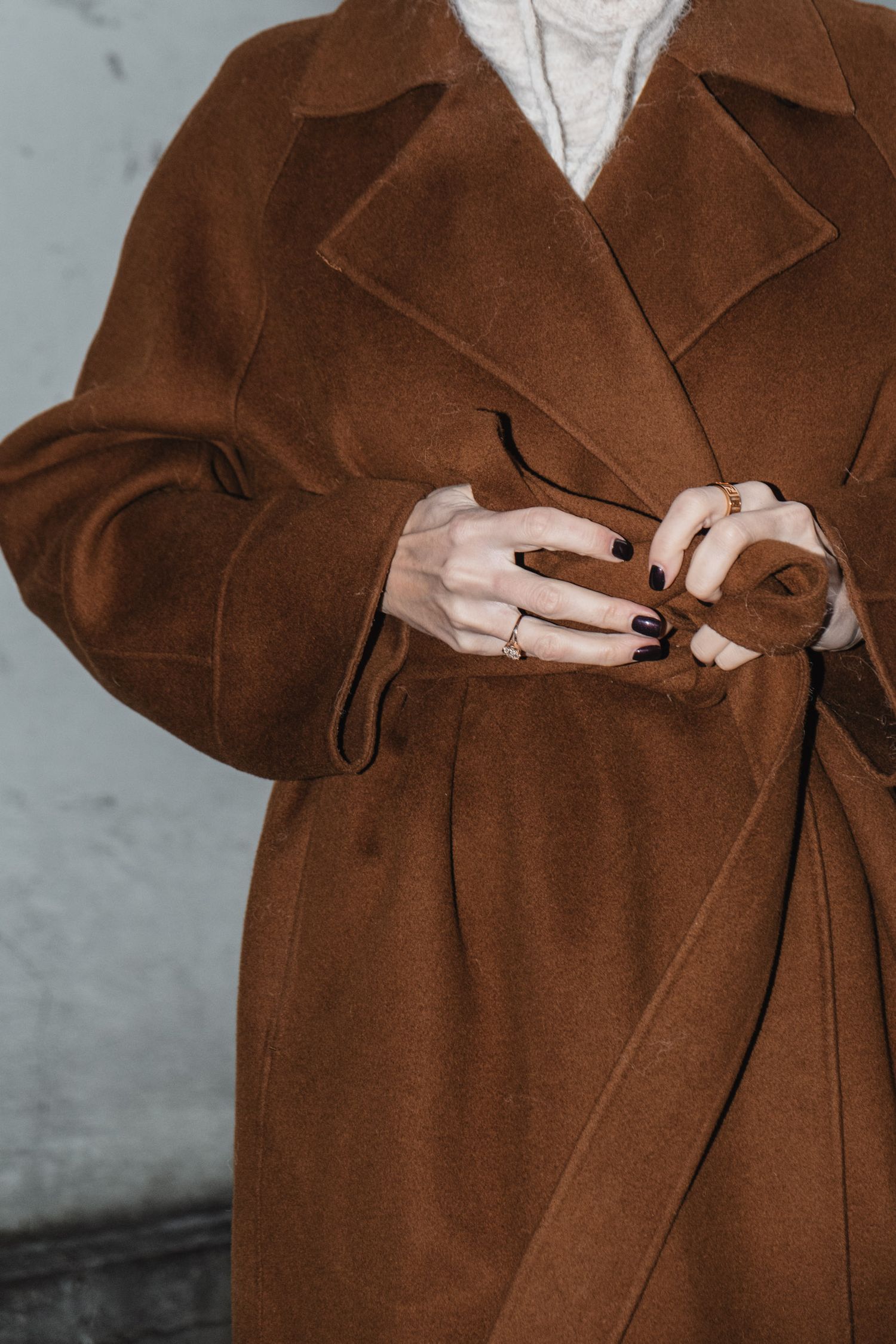 Close-up of hands with dark nail polish holding a brown wool coat belt.