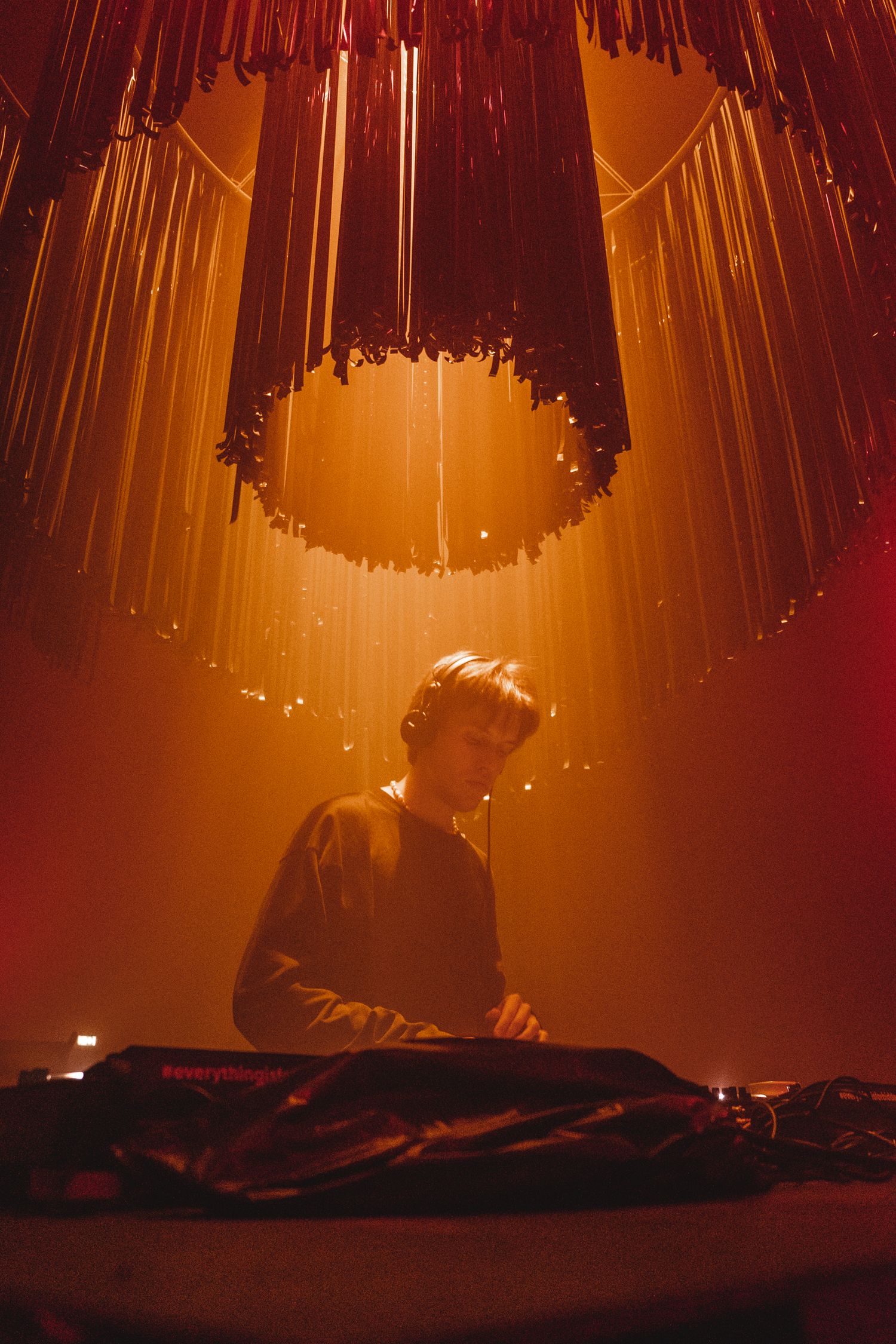 Dramatic orange stage lighting creates beams through smoke at a performance venue.