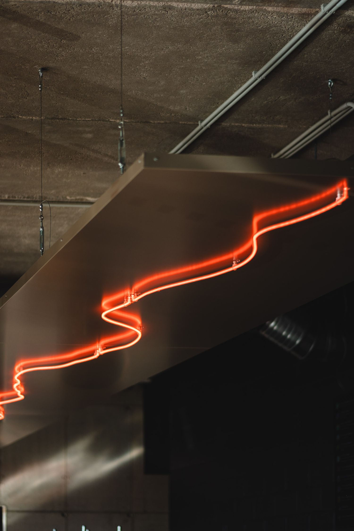 Red neon light installation zigzagging across a dark industrial ceiling.