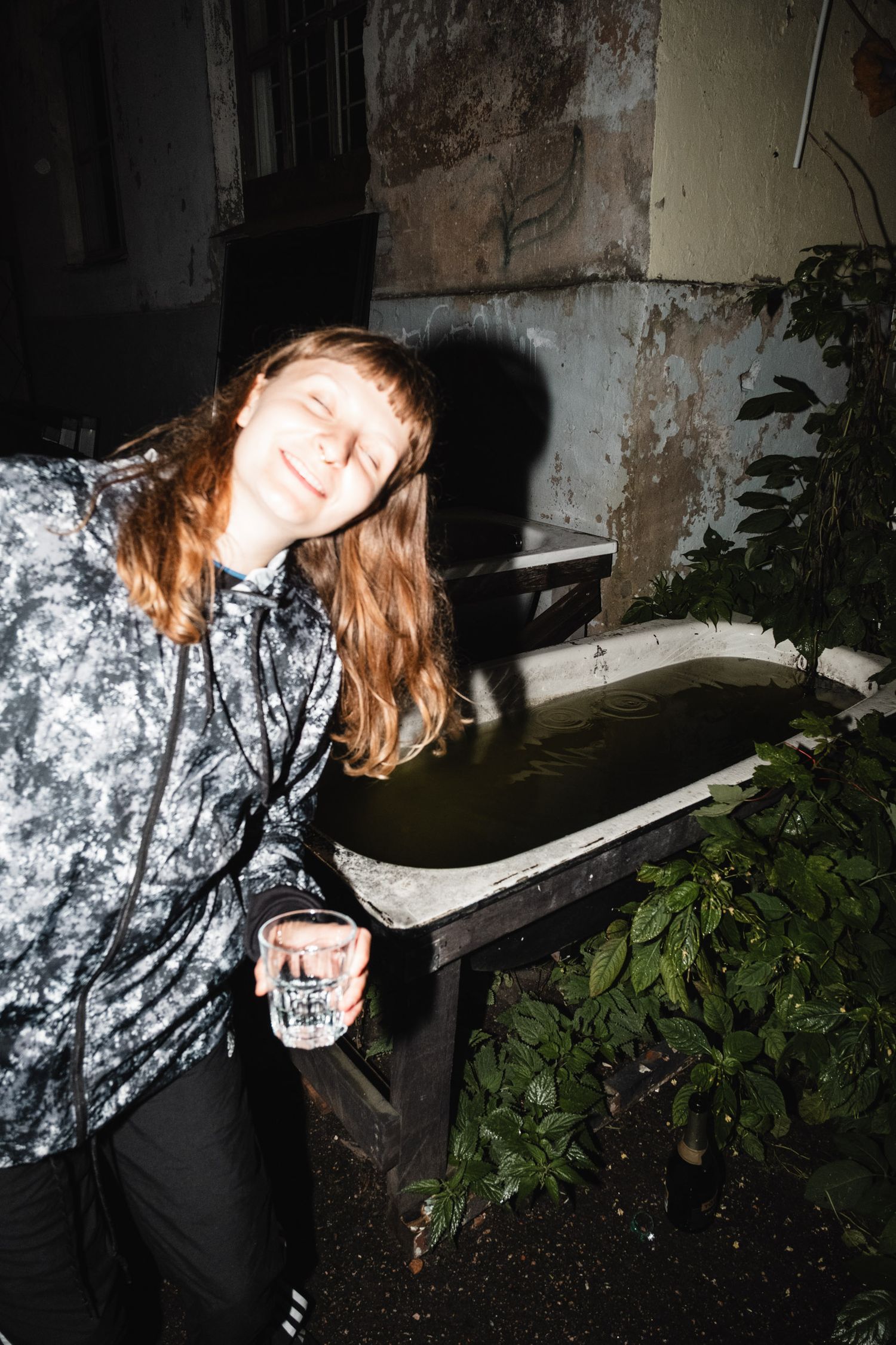 Person in patterned clothing bending down near plants in low light.