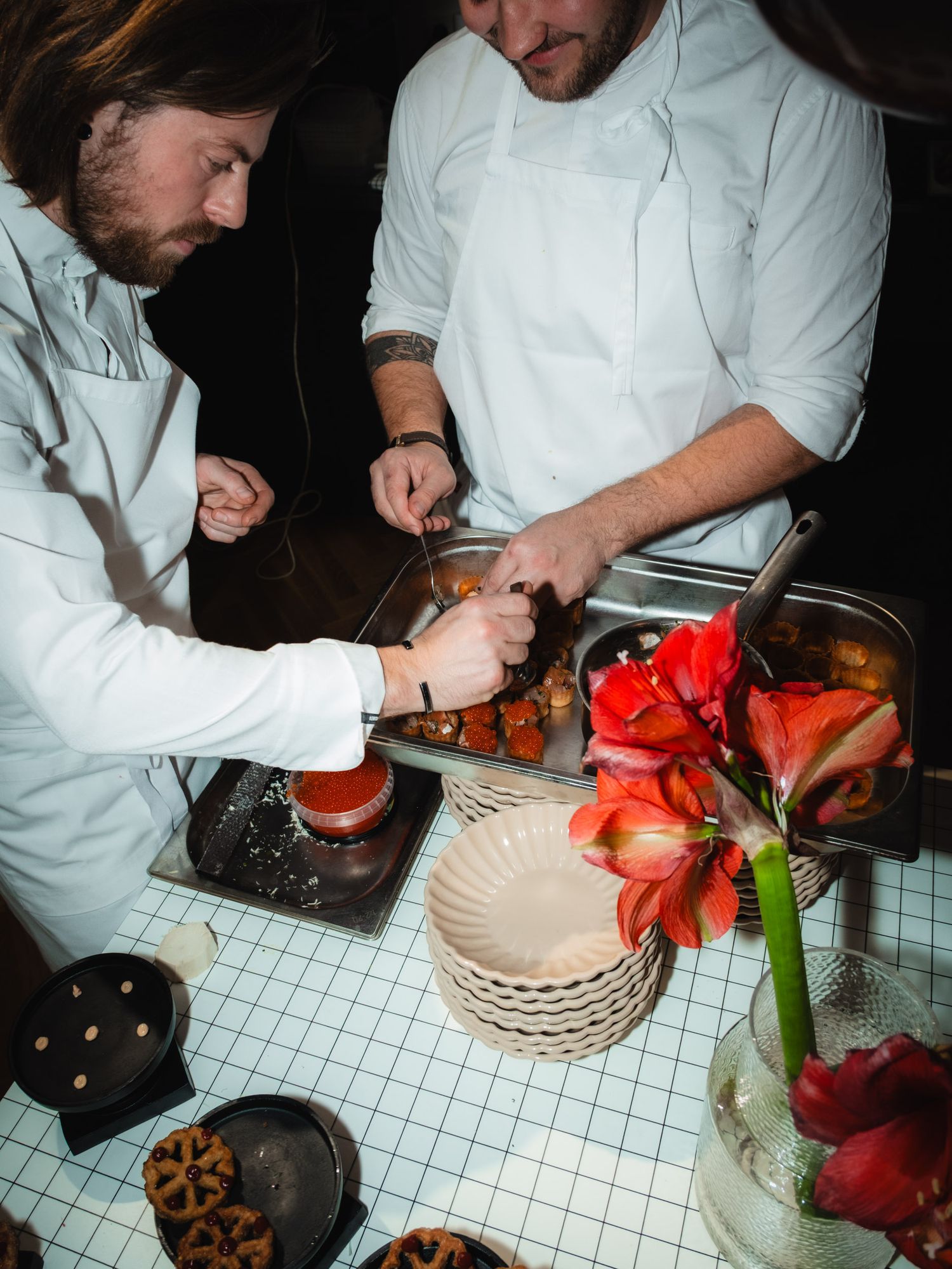 Chef in white uniform preparing fresh red bell peppers and ingredients on a tiled kitchen counter surface.