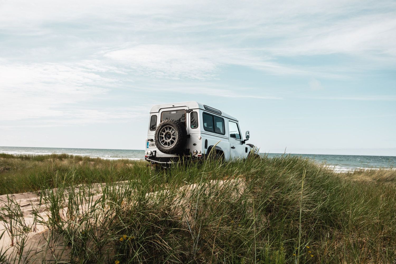 Land Rover Defender parked on coastal dunes with ocean view.
