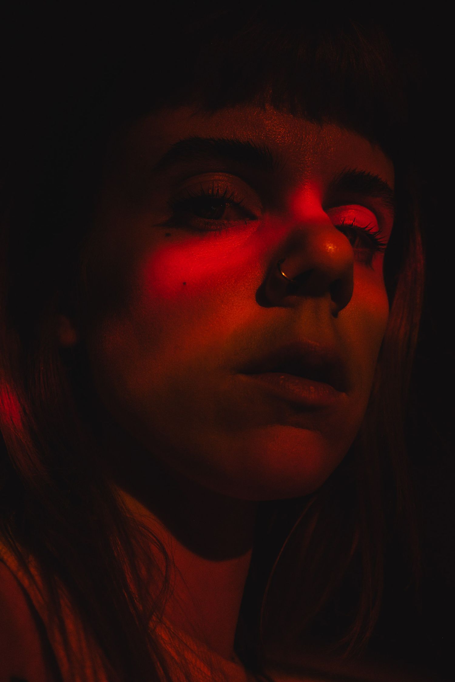 Close-up portrait bathed in dramatic red lighting creating a moody atmosphere.