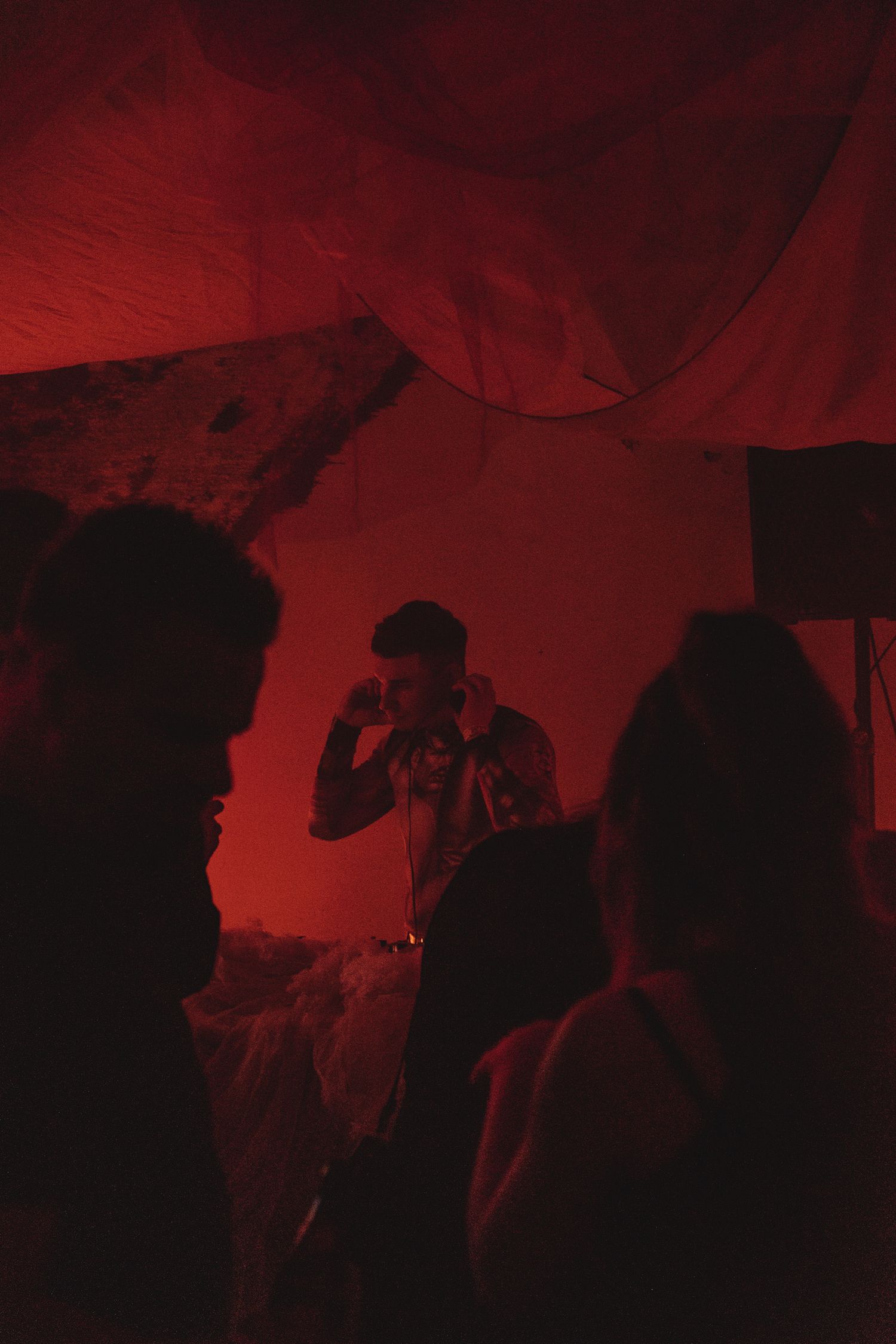 Silhouettes of people dancing in a dark room illuminated by red lighting at a nightclub party.