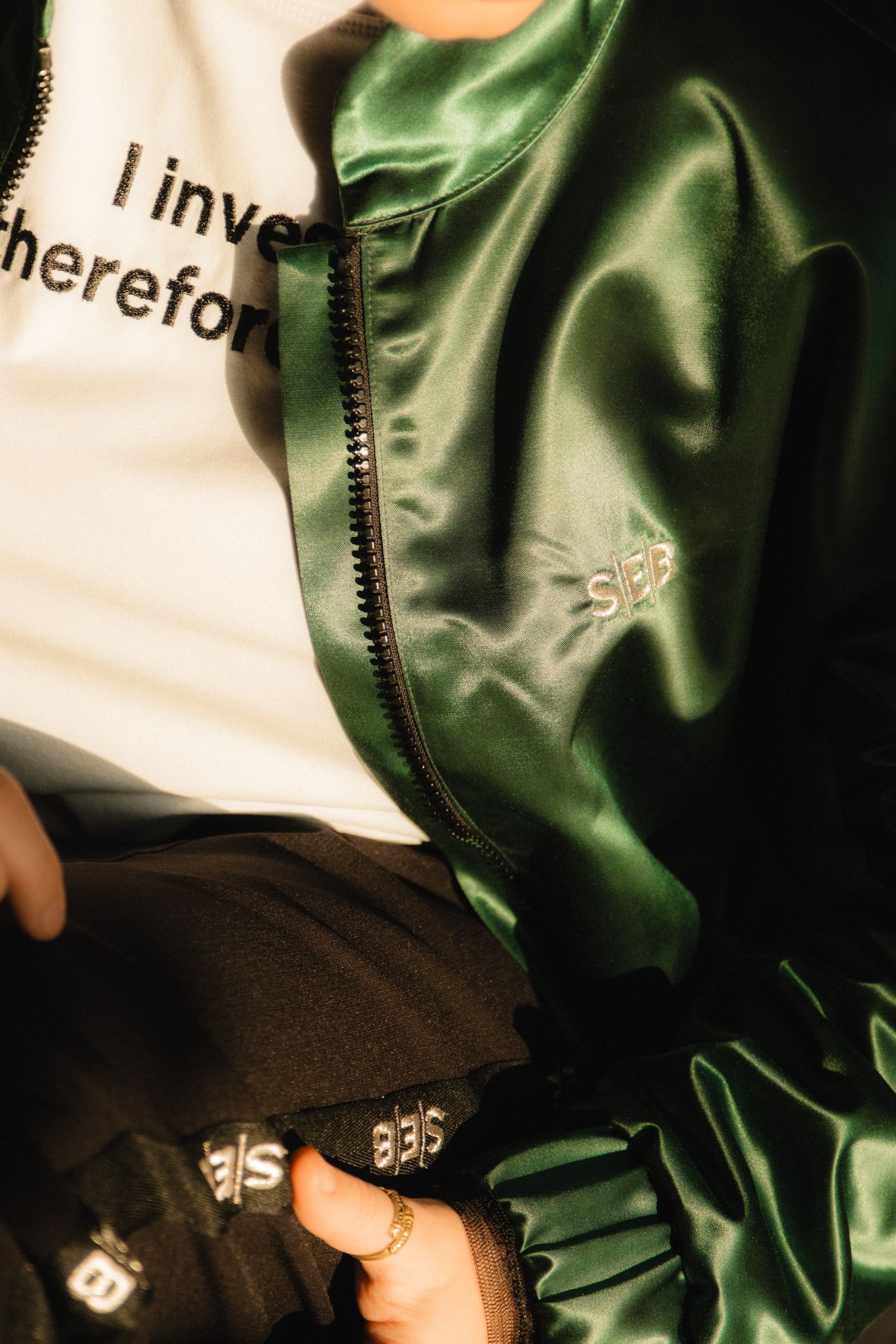 Close-up shot of a shiny green satin jacket with black zipper detail and text visible in the frame.