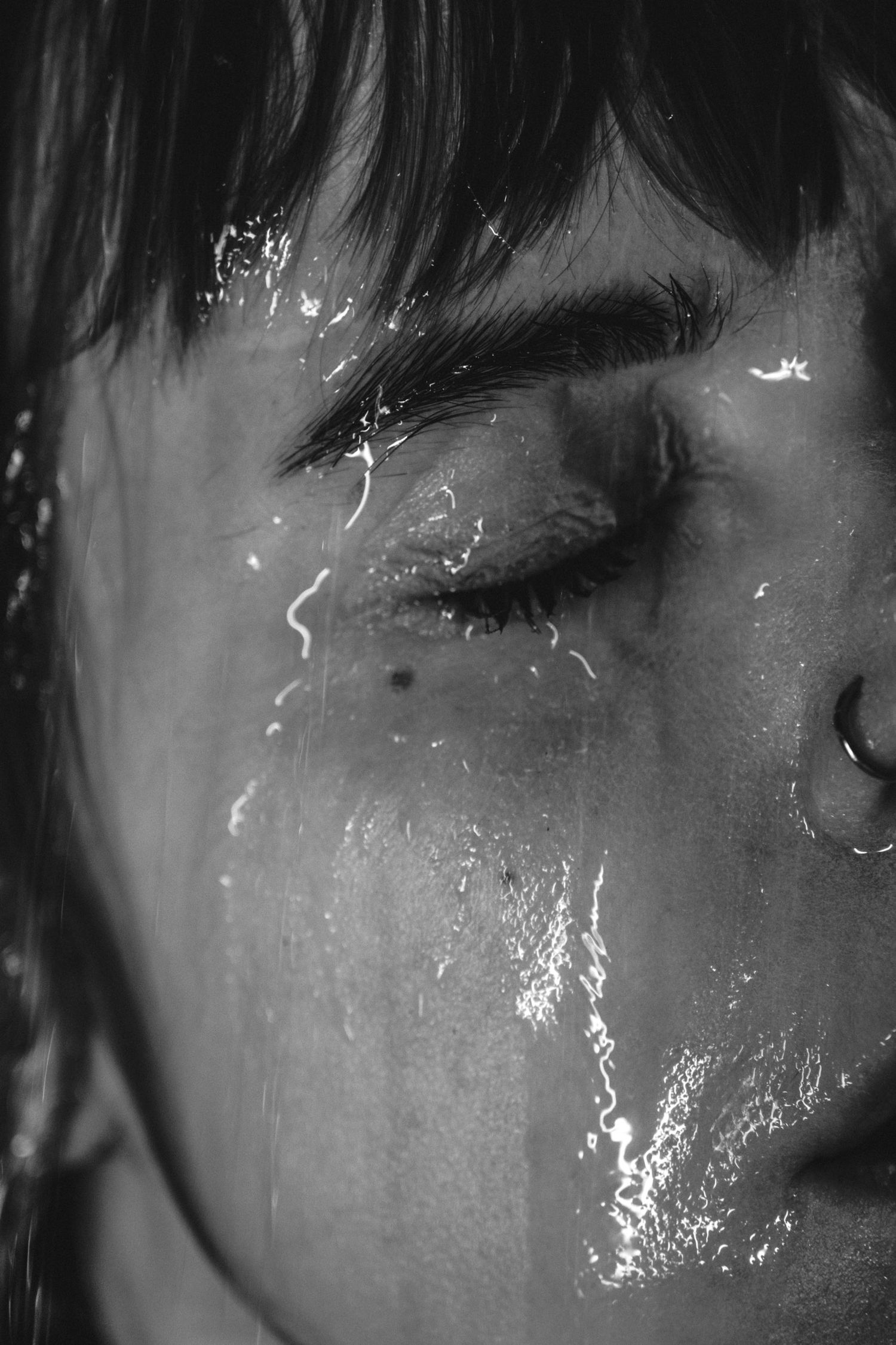 Close-up black and white portrait showing water droplets or tears on skin.