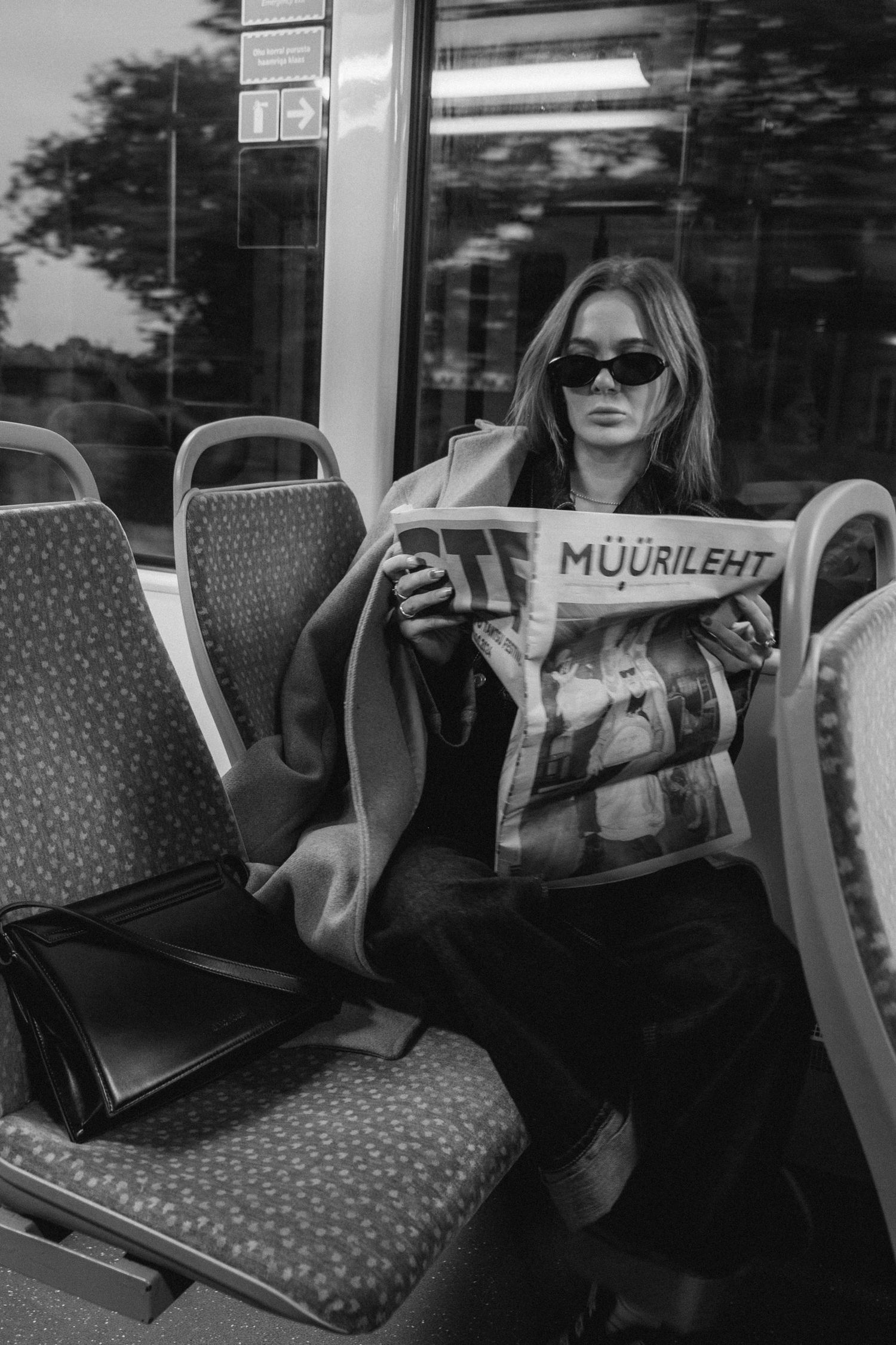 Person reading newspaper while sitting on patterned seats in public transport.