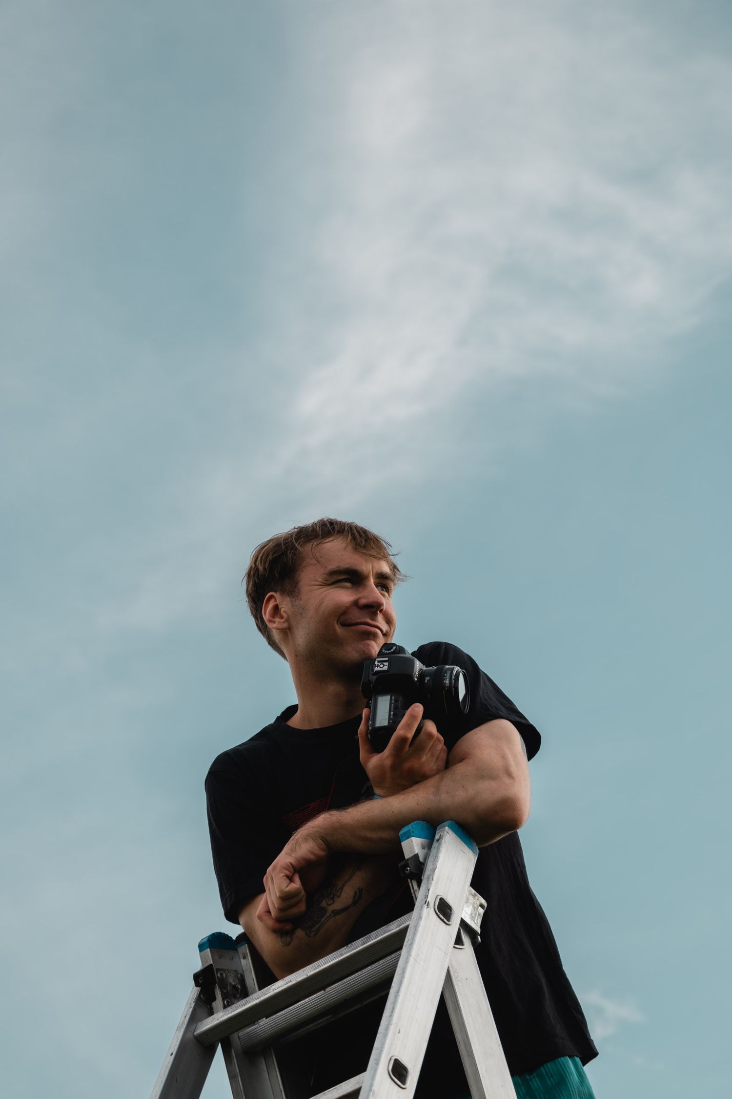 Low angle view of someone standing on a ladder against blue sky holding camera equipment.