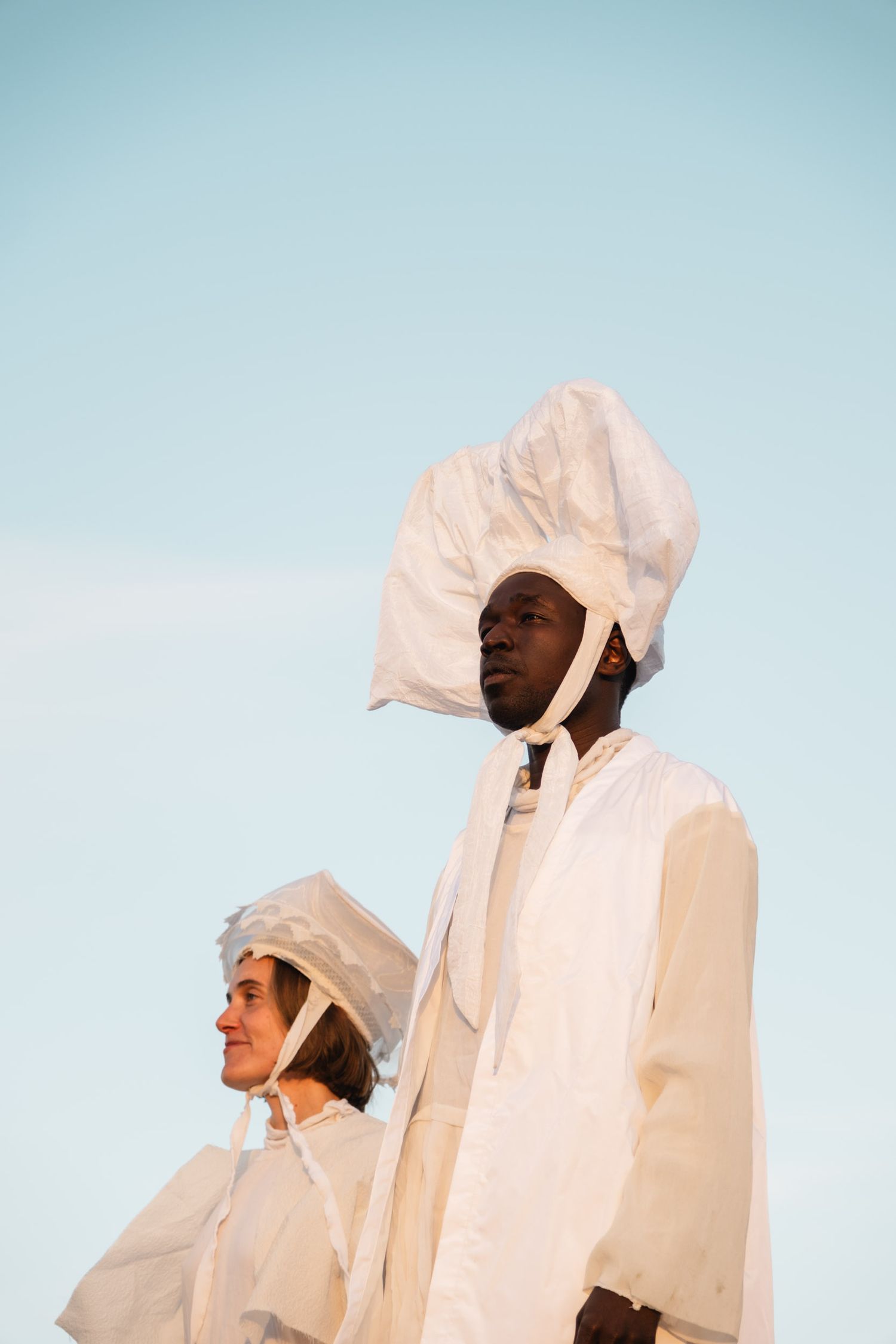 Group wearing white hooded garments pose against bright blue sky.