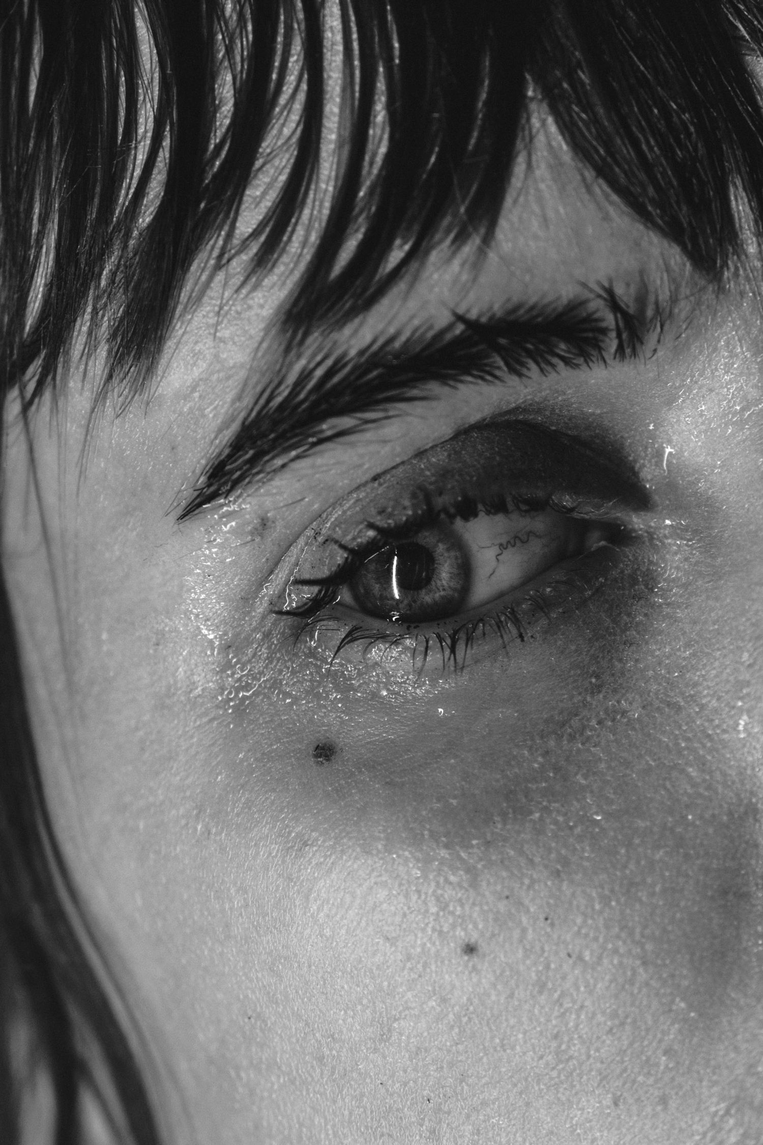 Extreme close-up black and white photograph of an eye with dark bangs framing the shot.