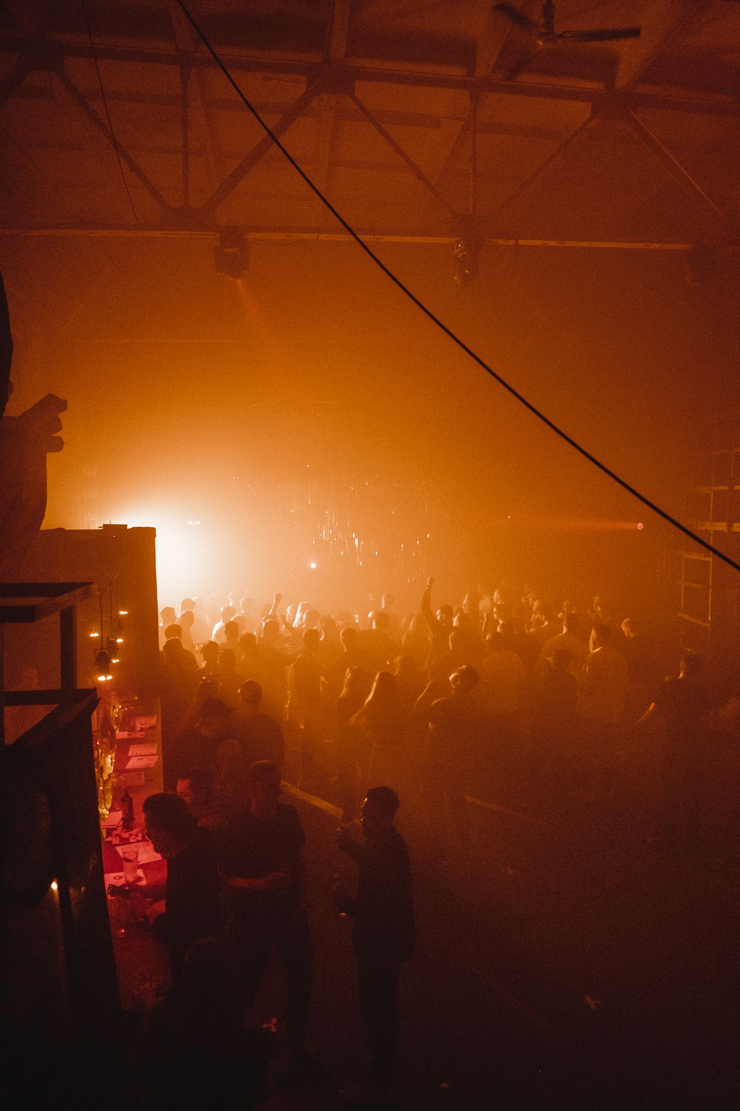 Hazy orange-lit concert venue filled with a standing crowd.
