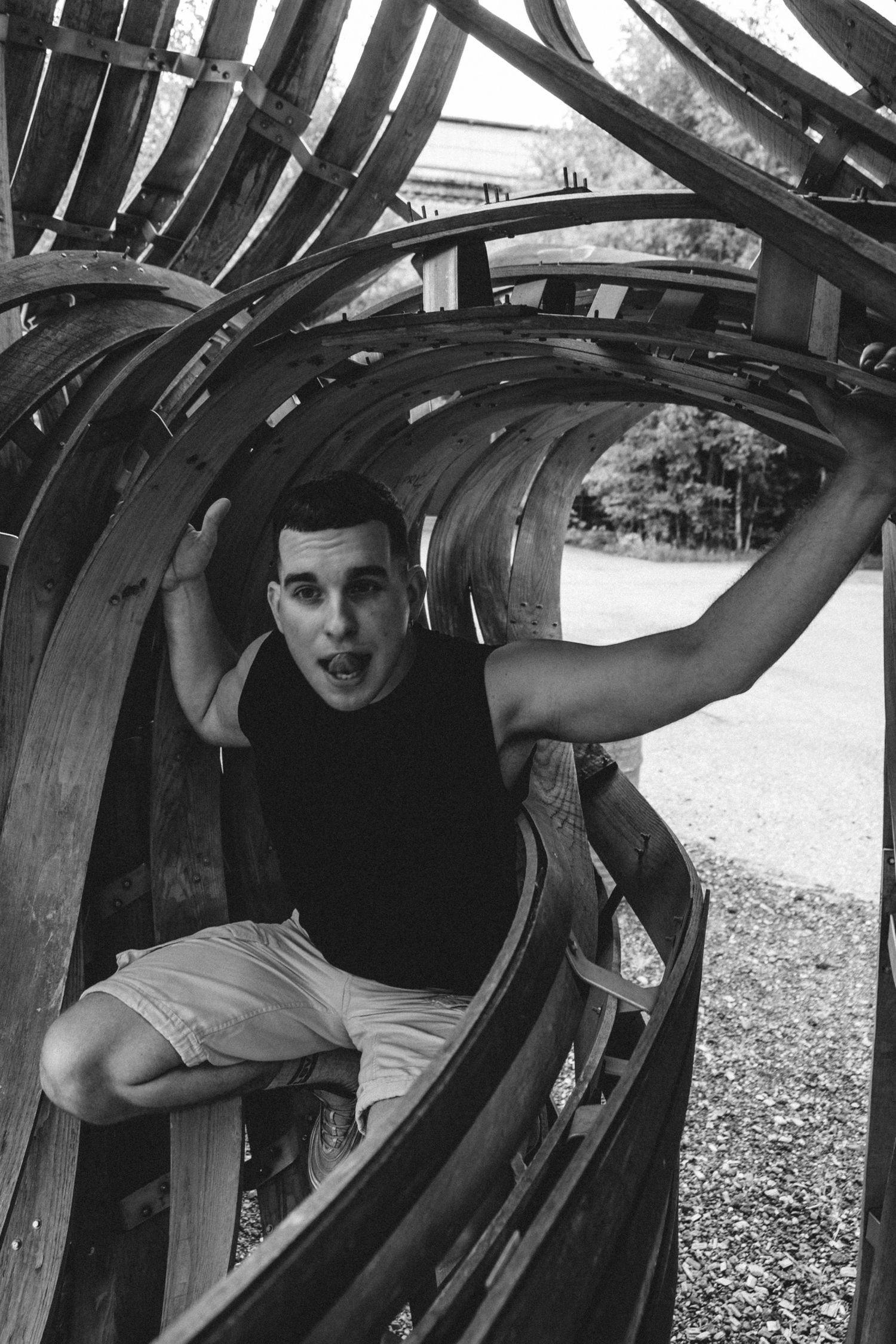 Person poses inside curved wooden playground equipment structure in black and white photography.