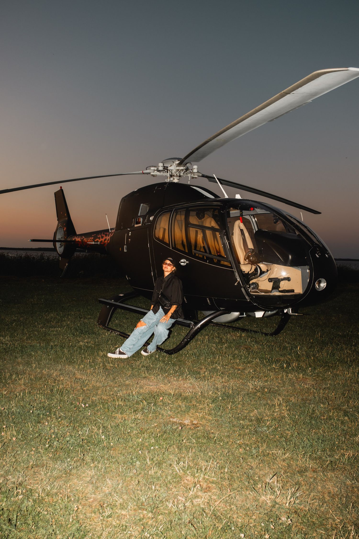 Black helicopter parked on grassy field during sunset.