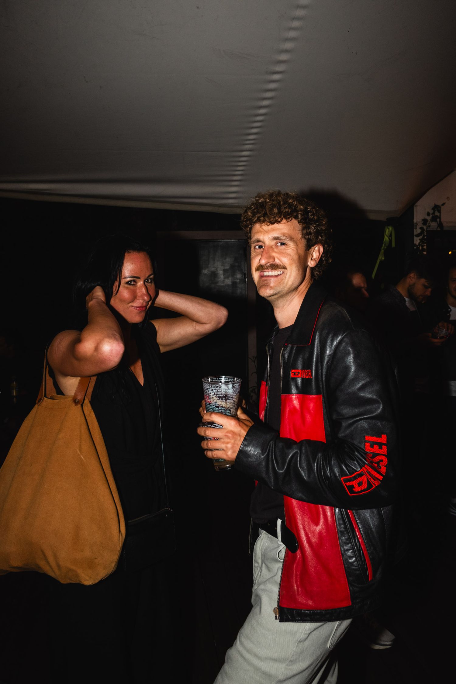 People socializing at a dimly lit party with drinks and casual attire.