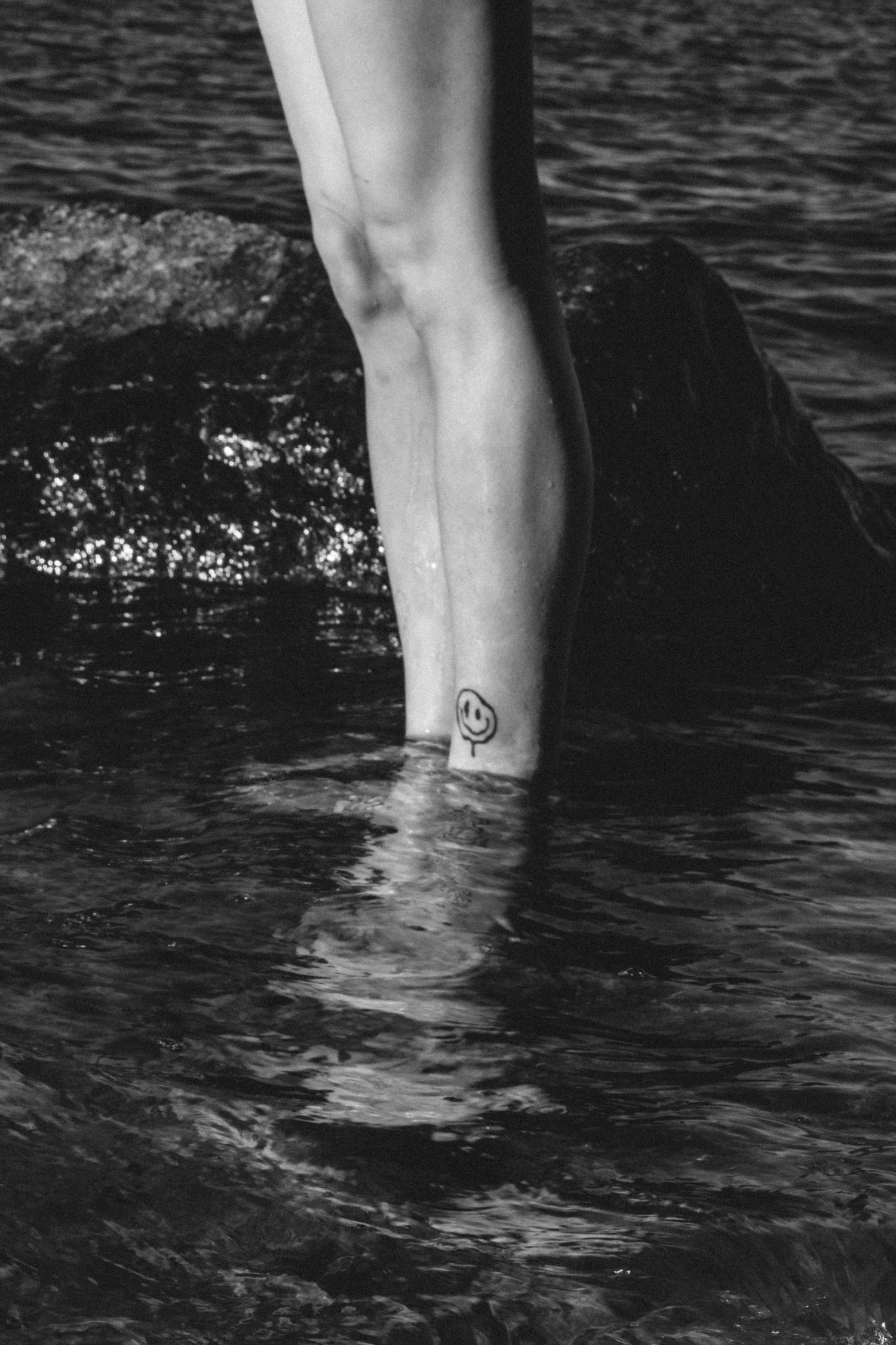 Black and white close-up of legs wading in dark rippling water.