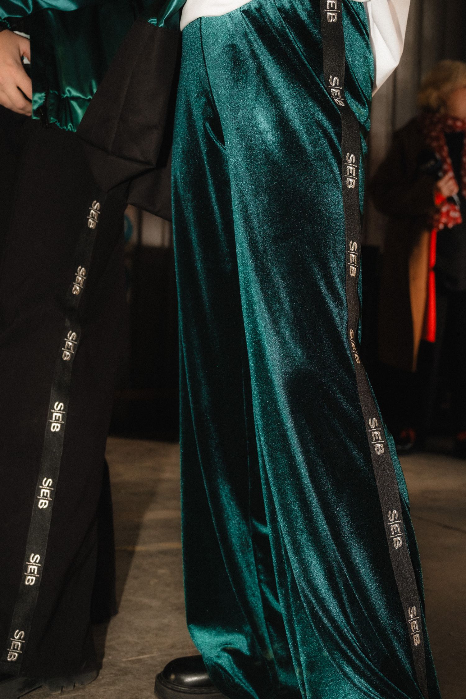 Emerald green velvet dress with black trim and ornate silver buttons shown on display at fashion event.