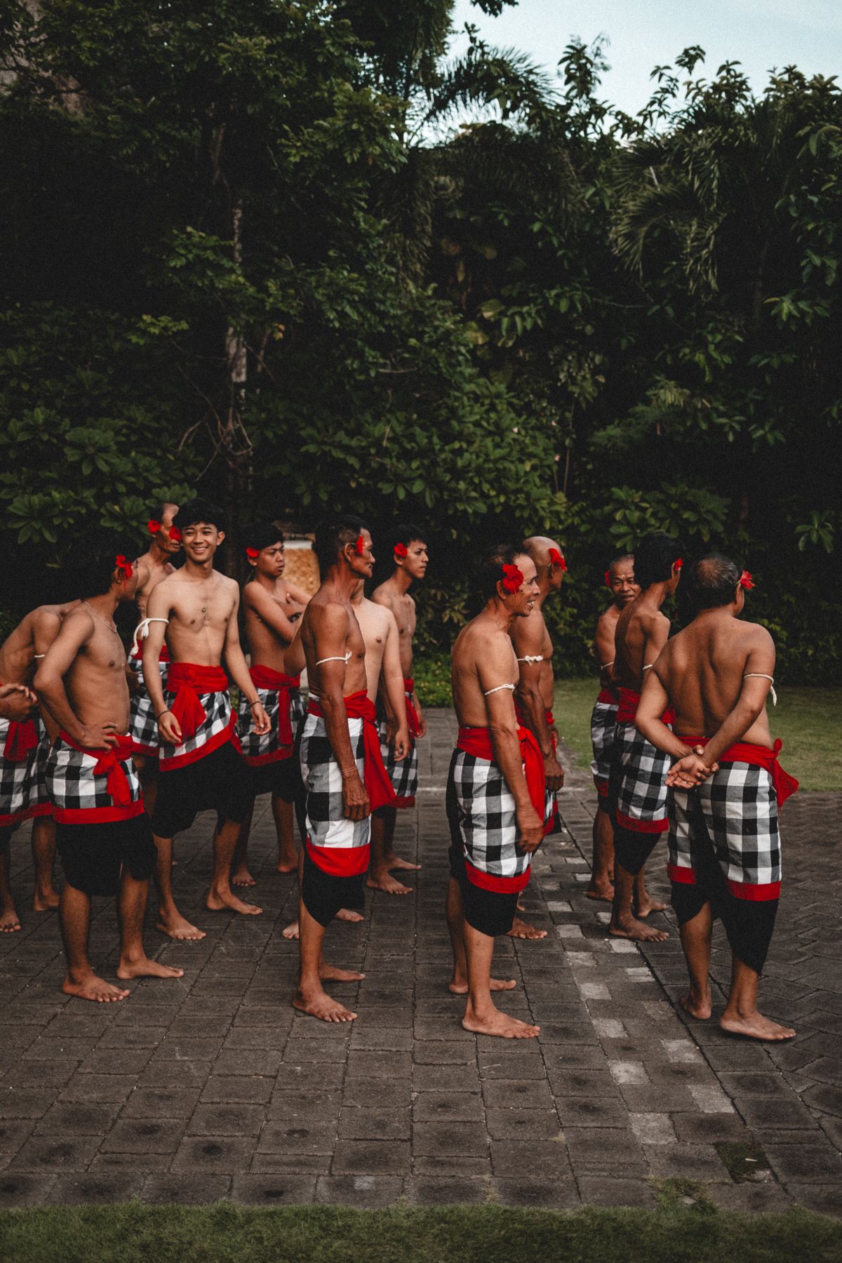 Group wearing traditional Balinese sarongs standing in formation on stone pathway.