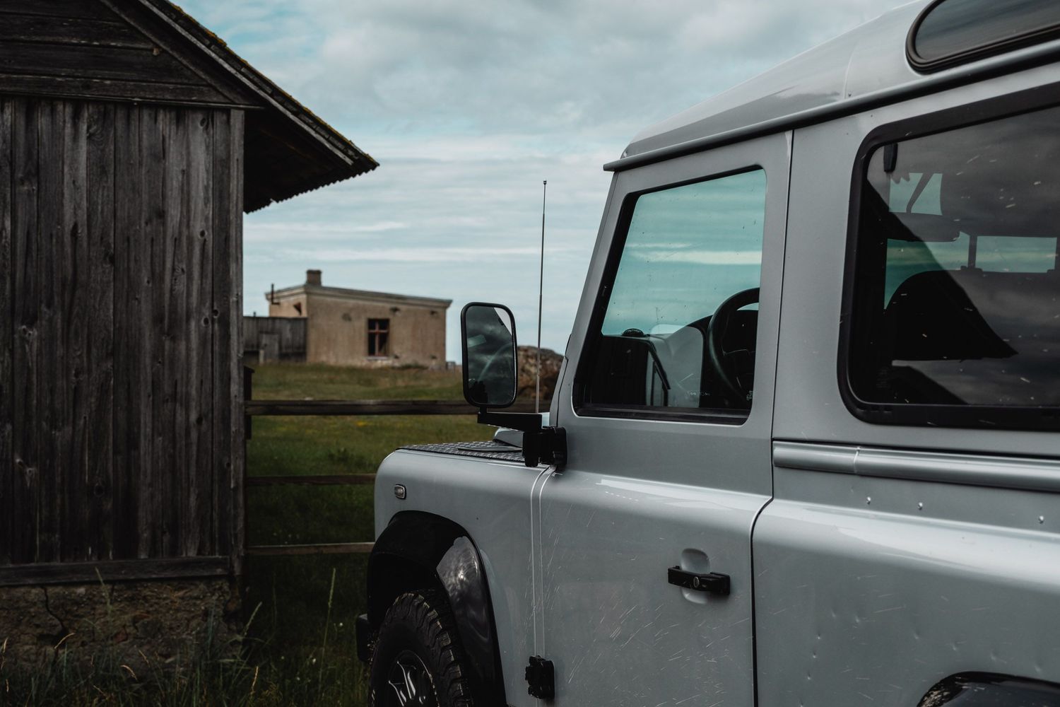 Collection of vintage Land Rover vehicles parked near rustic wooden buildings.