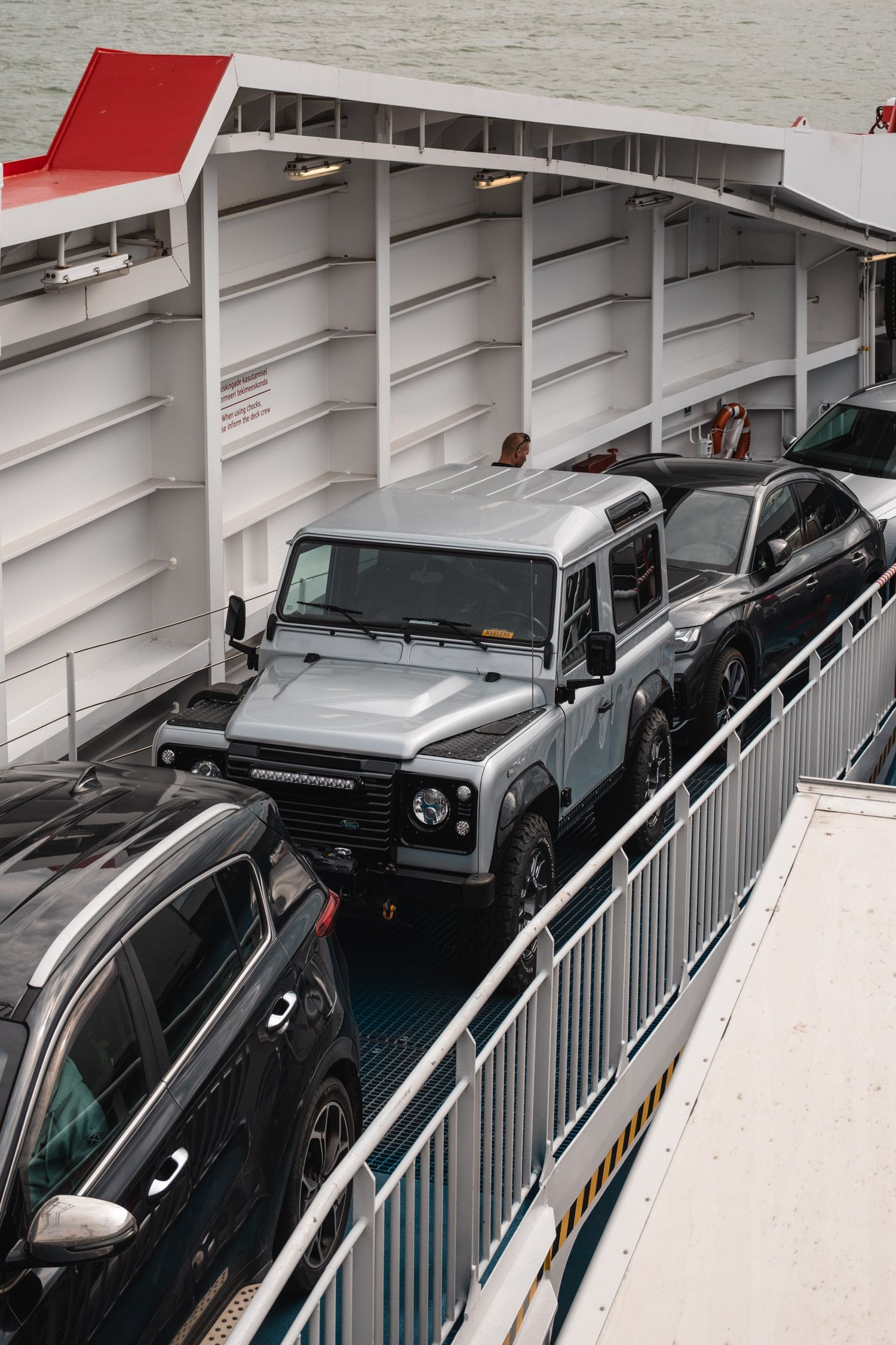 Row of parked vehicles on a ferry deck with metal railings and white ceiling structure.