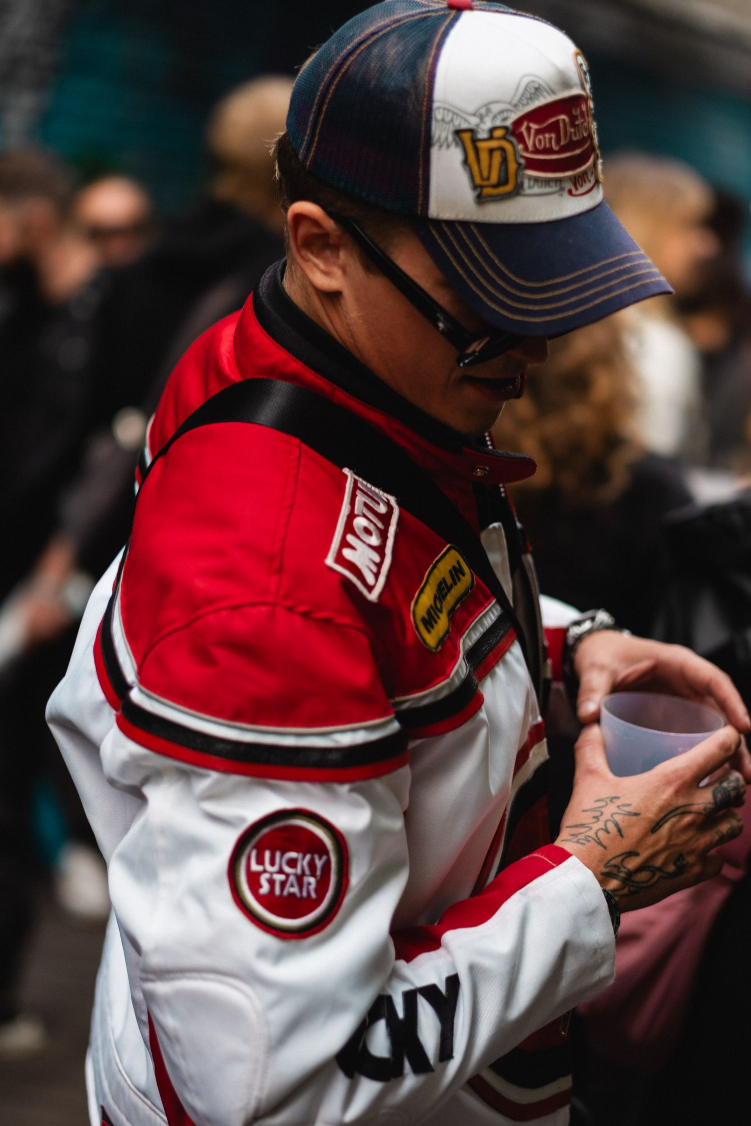 Person wearing a red and white sports jacket with Lucky You patches and a baseball cap.