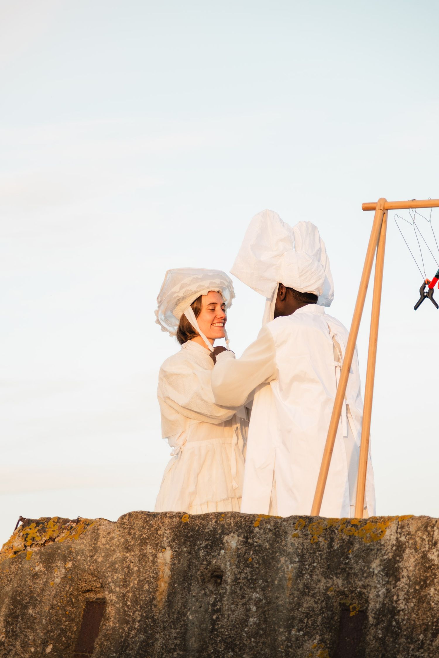 Figures in white costumes perform on a concrete wall against bright sky.