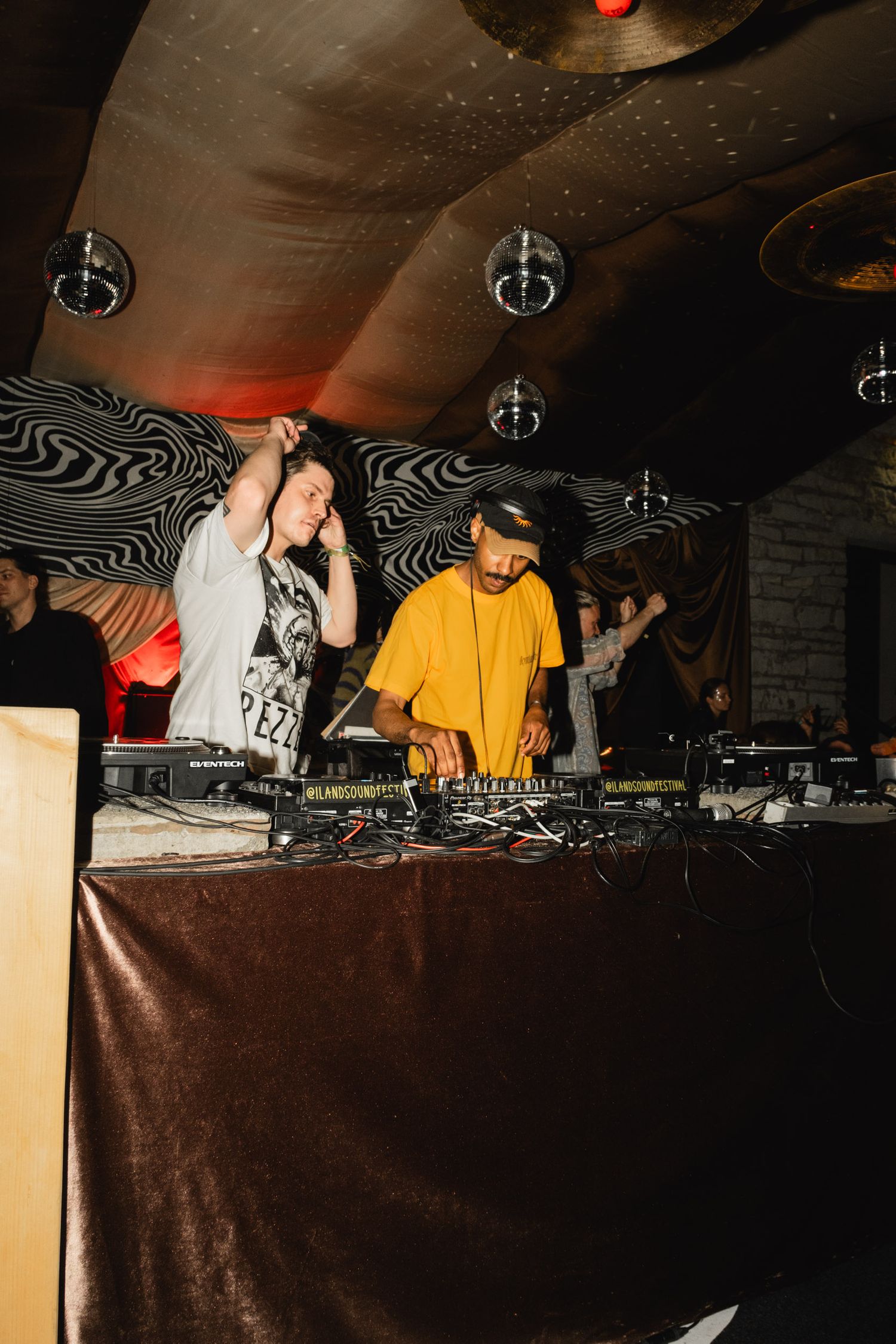 DJs performing at a nightclub with turntables and mixing equipment under moody lighting.
