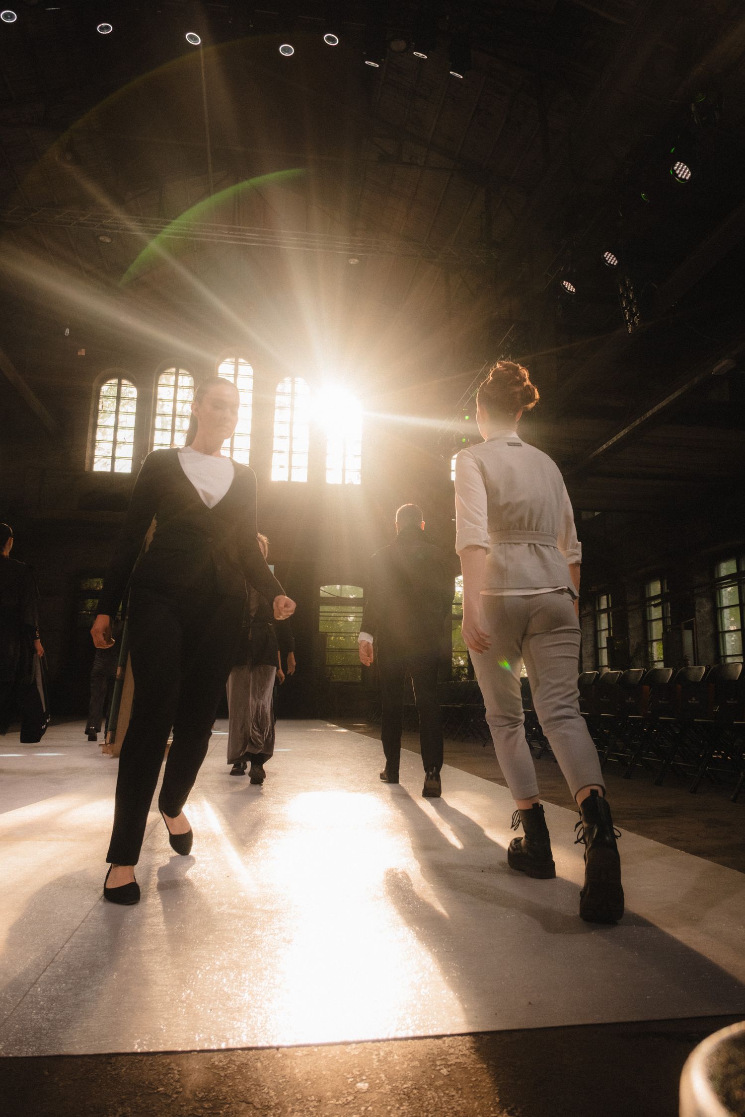Models silhouetted against bright sunlight streaming through windows on a catwalk.