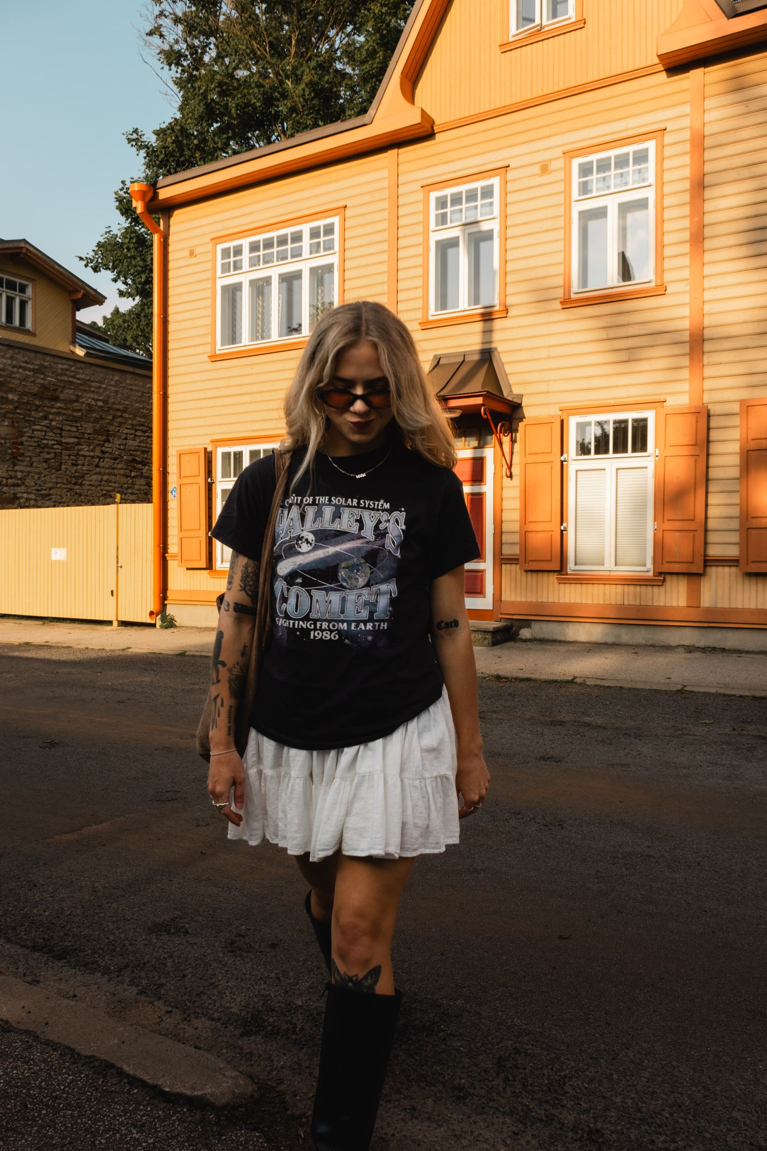 A casual street style outfit featuring a graphic t-shirt and white skirt against an orange building.