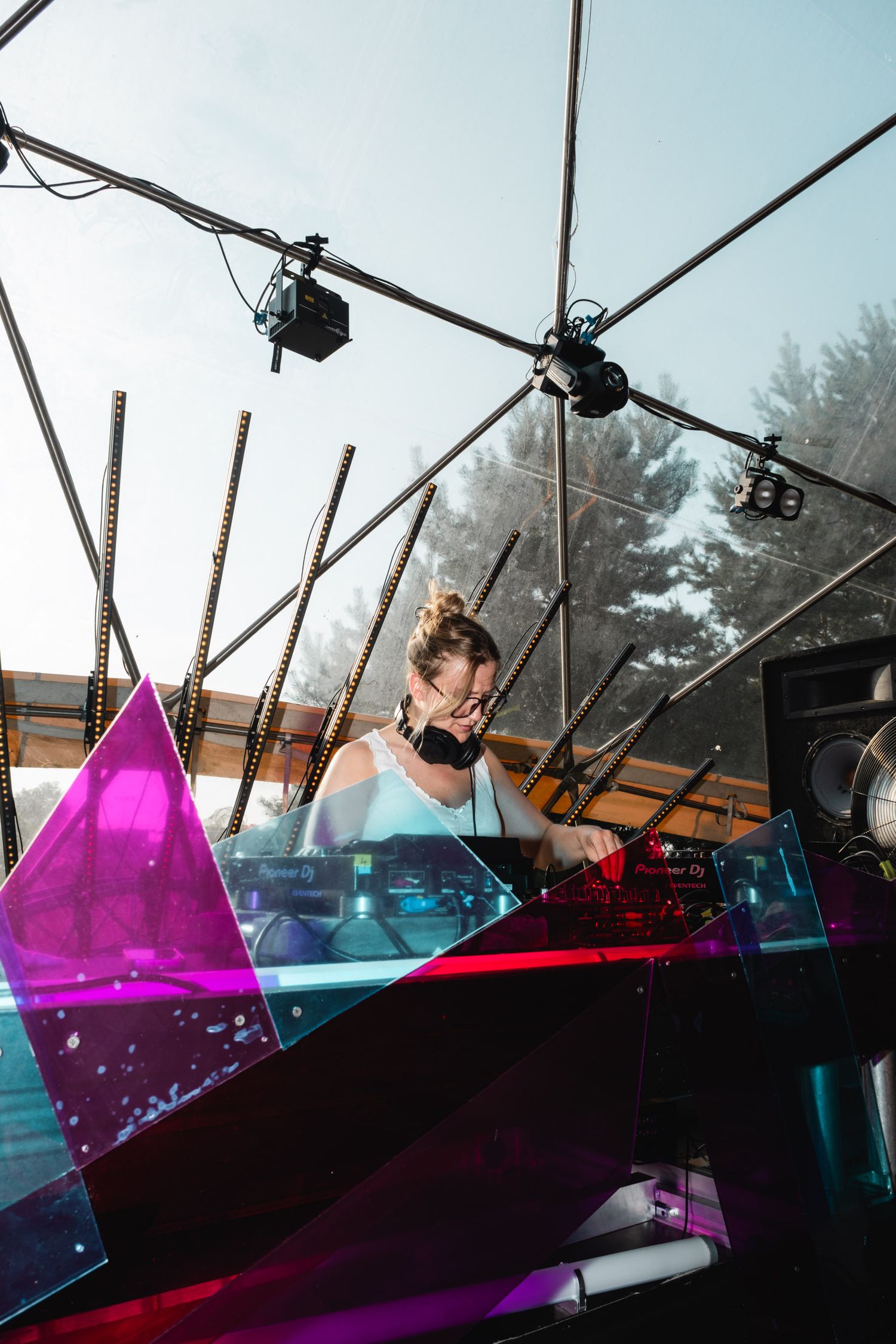 DJ performing at outdoor event with colorful geometric stage design and lighting equipment.