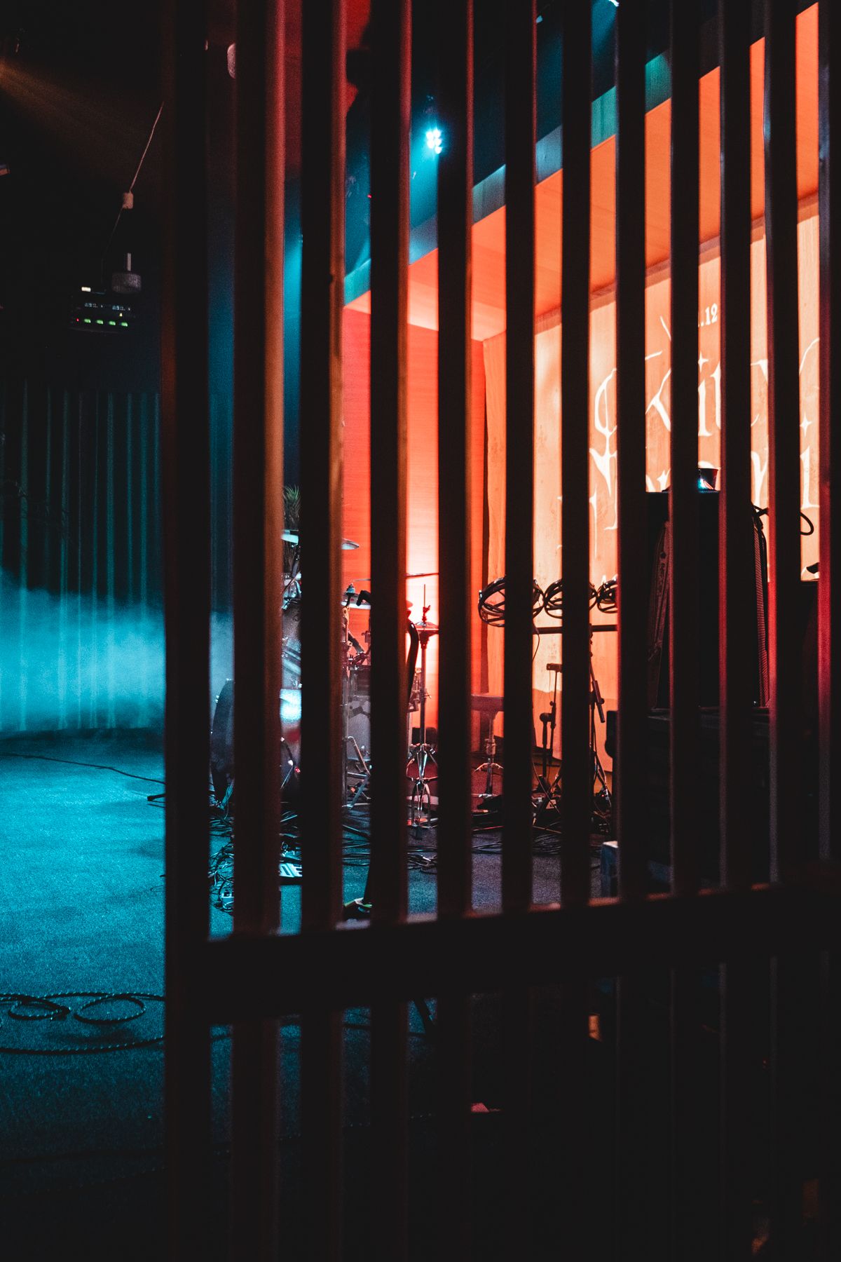 Colorful stage lighting creates blue and orange stripes through vertical bars in dark concert venue.