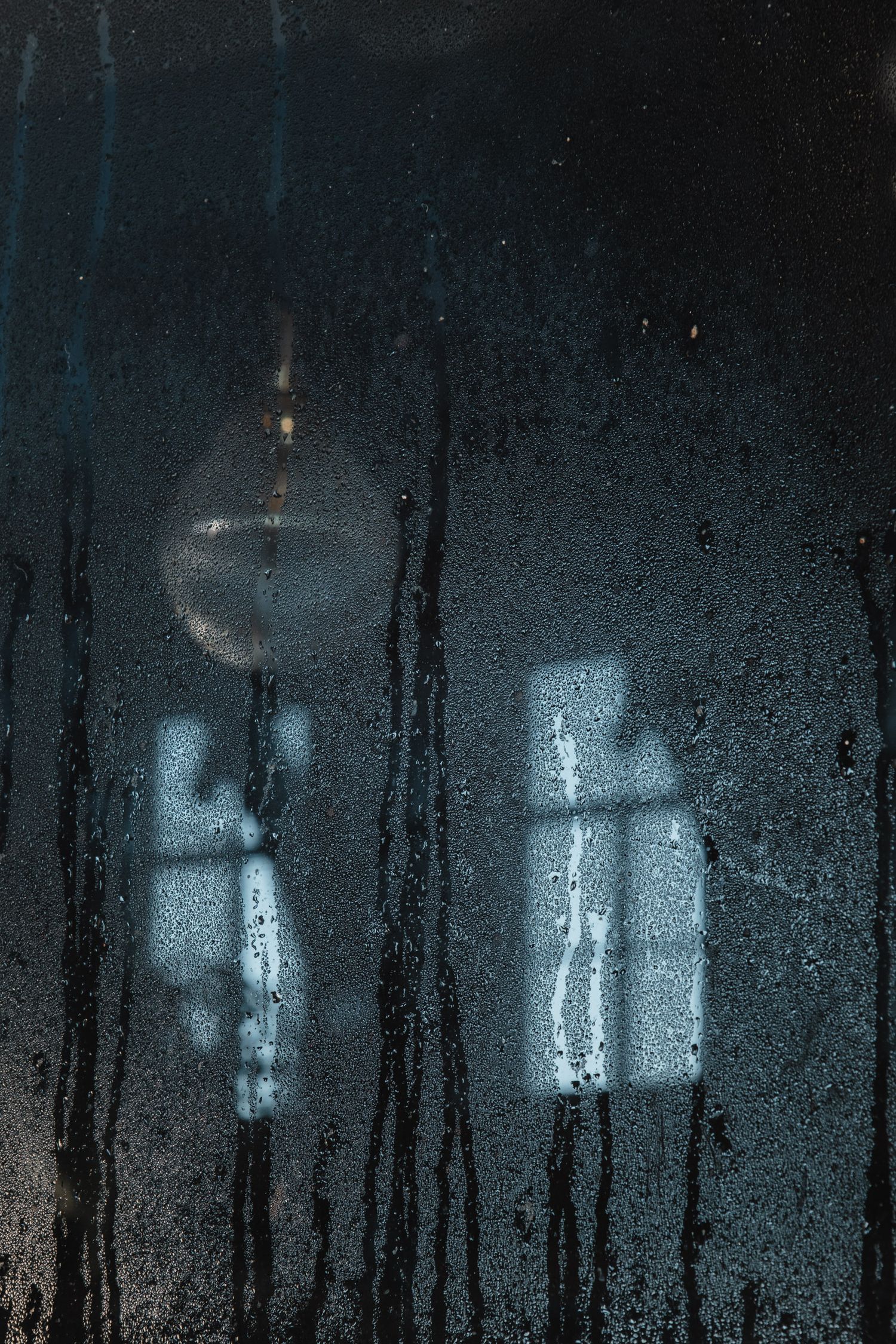 Eerie window reflections through condensation create ghostly shapes in dark atmosphere.