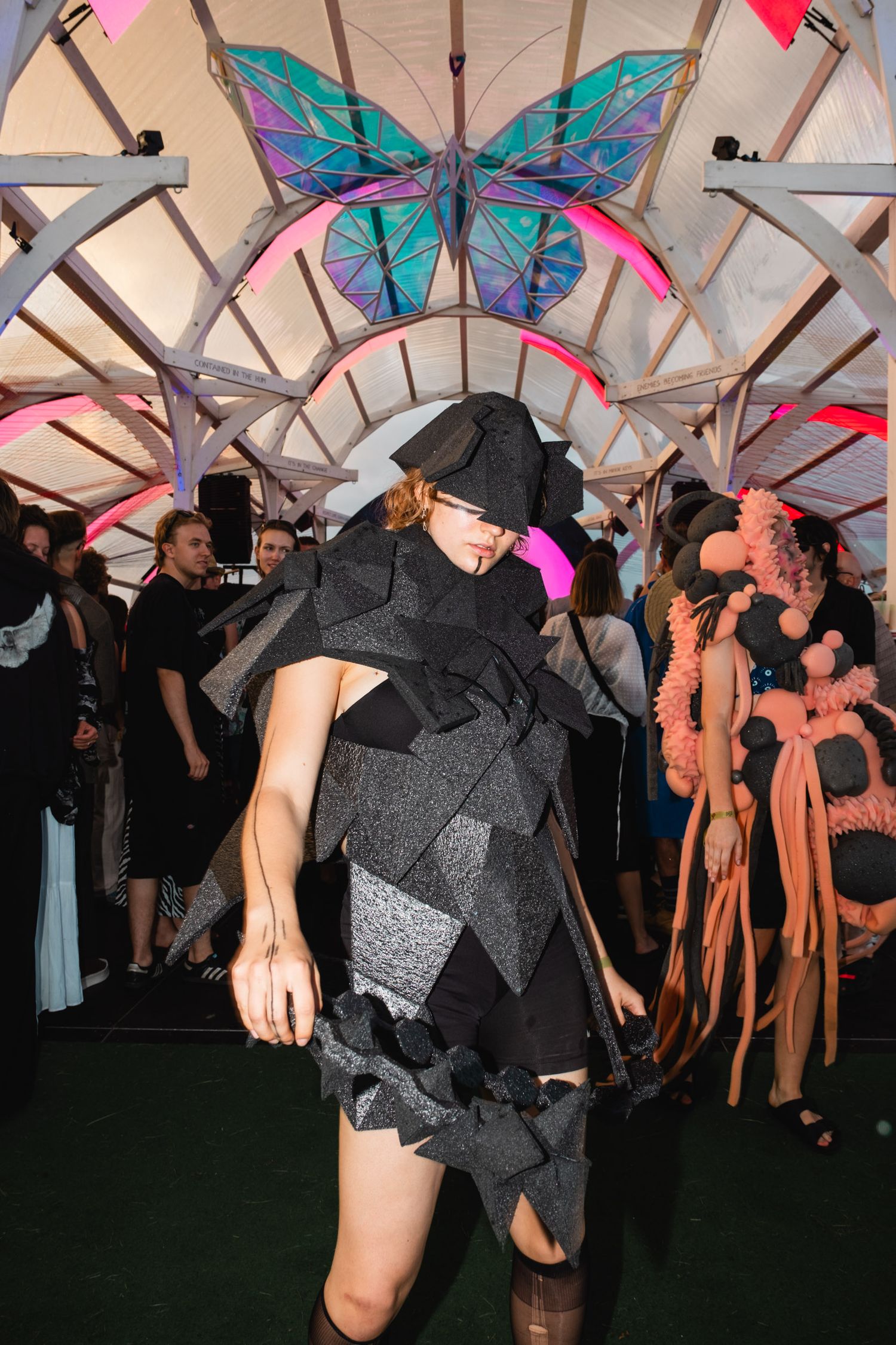 Festival crowd under geometric canopy with butterfly decorations.