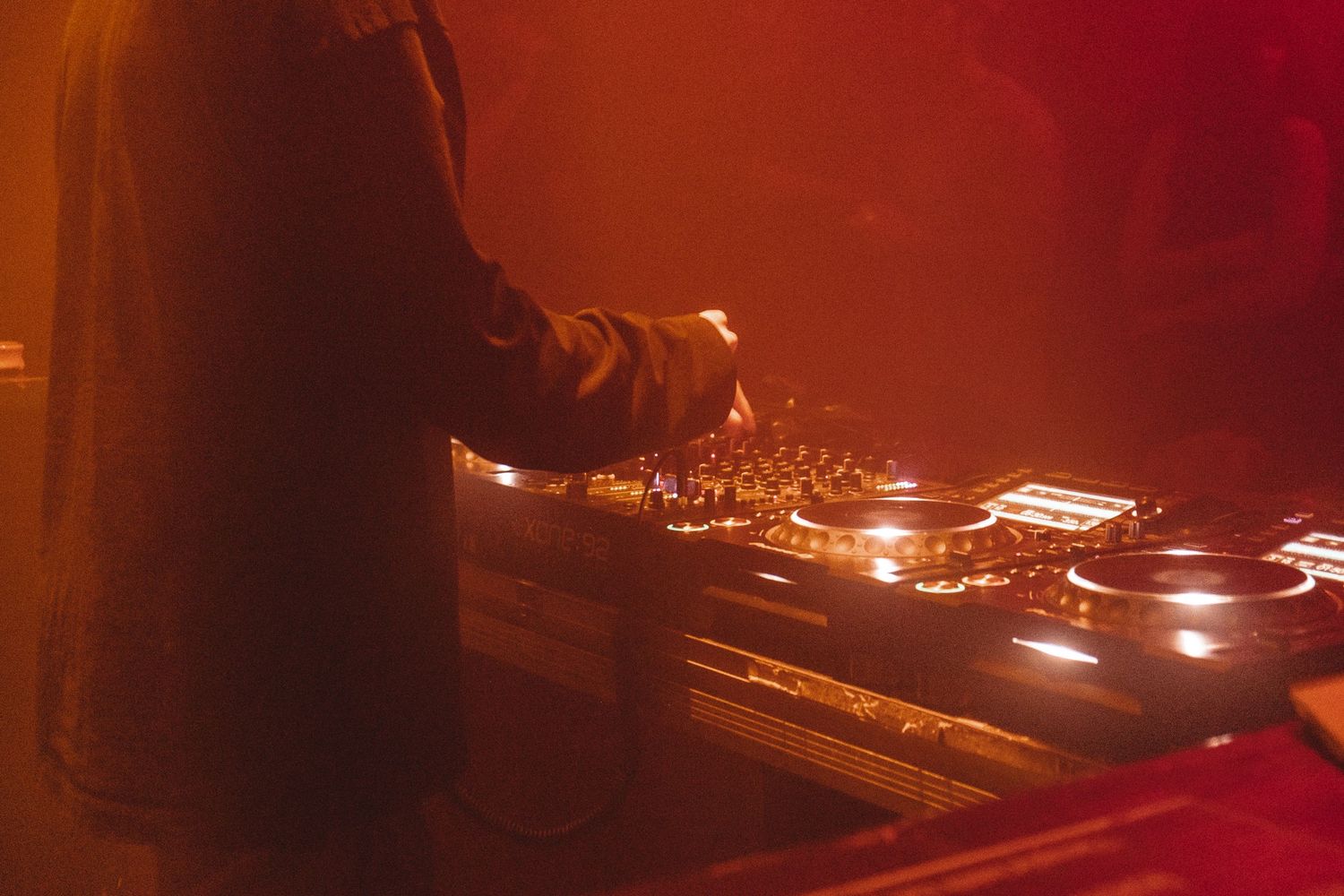 DJ equipment and turntables illuminated by warm red stage lighting.