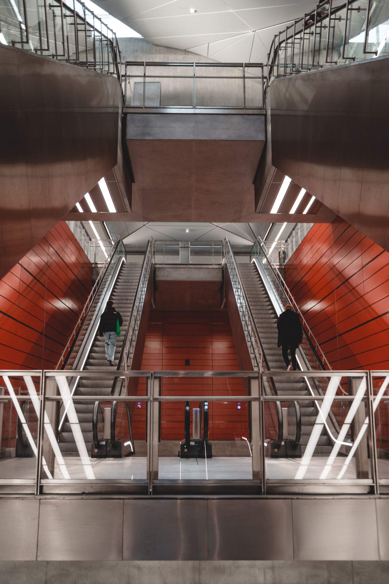 Modern subway station interior with red walls and stainless steel escalators.