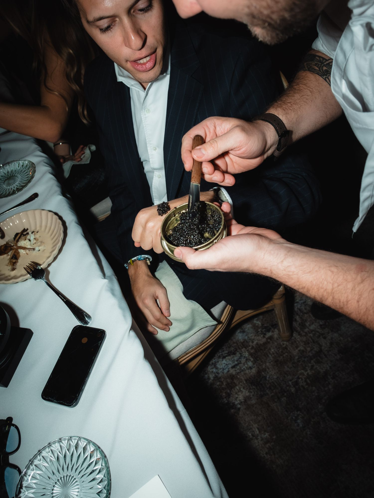 People examining caviar or black fish roe being served at an elegant dining table with crystal glassware.