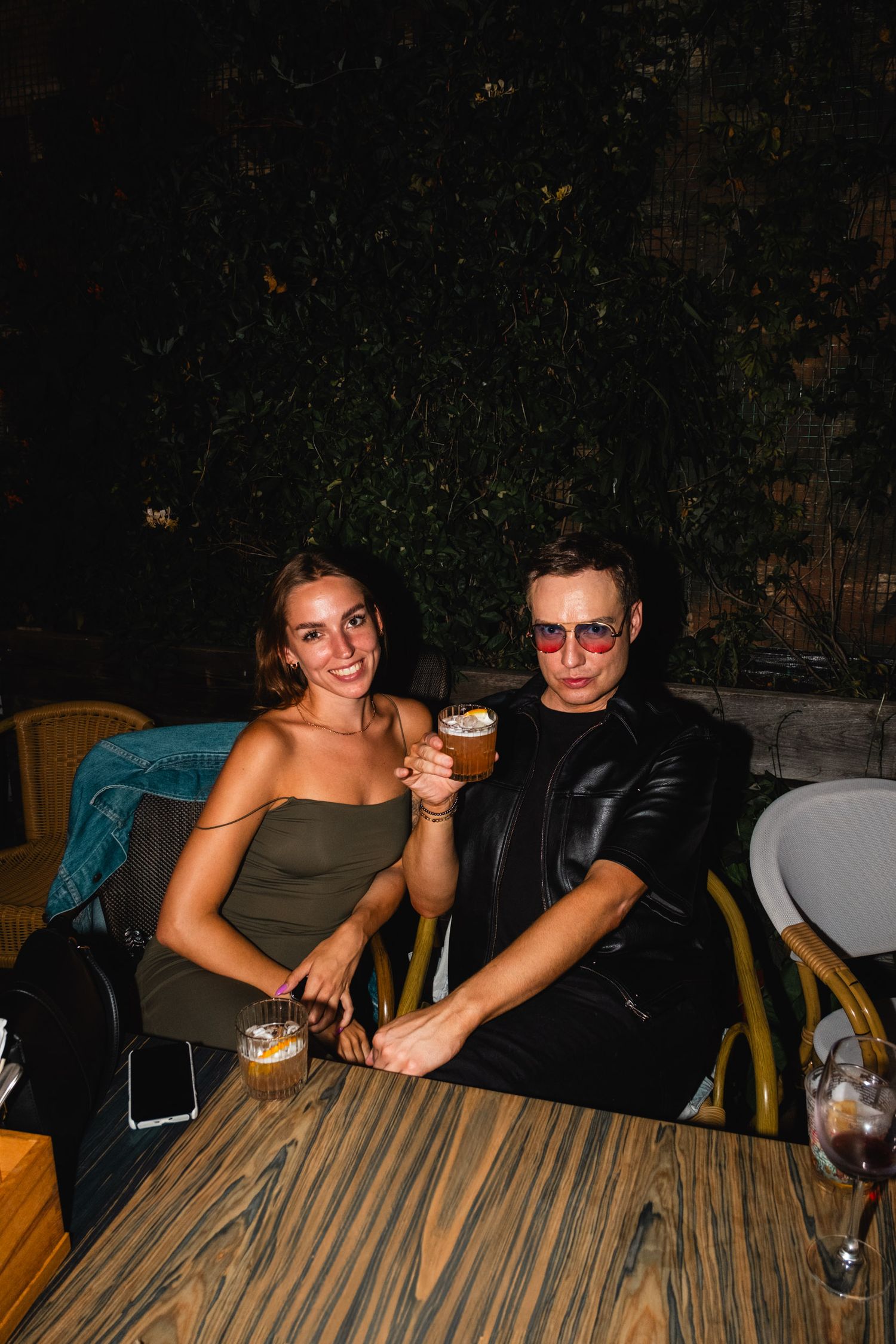 Couple enjoying drinks at outdoor table during nighttime gathering.