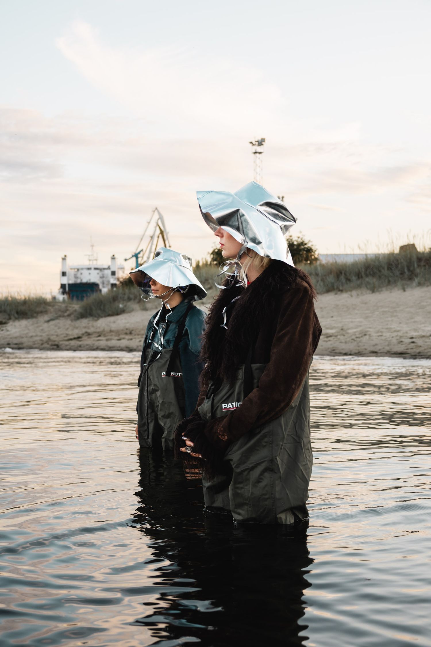People wearing reflective masks stand in shallow water at sunset.