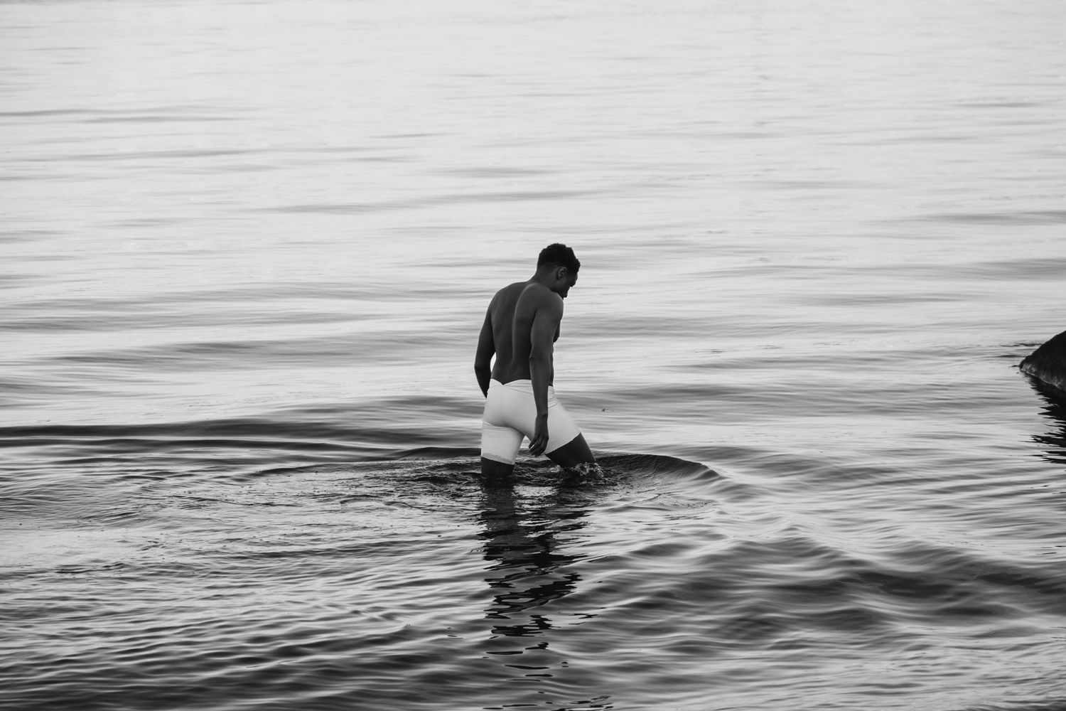 Silhouettes of people wading in calm ocean waters at dusk.