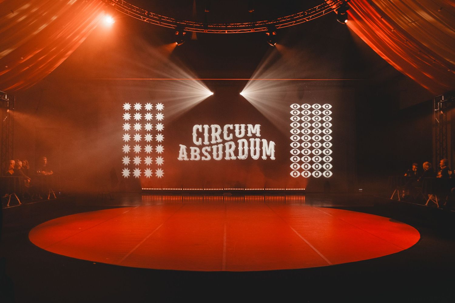 Wide shot of a circus stage with red lighting and illuminated signage.