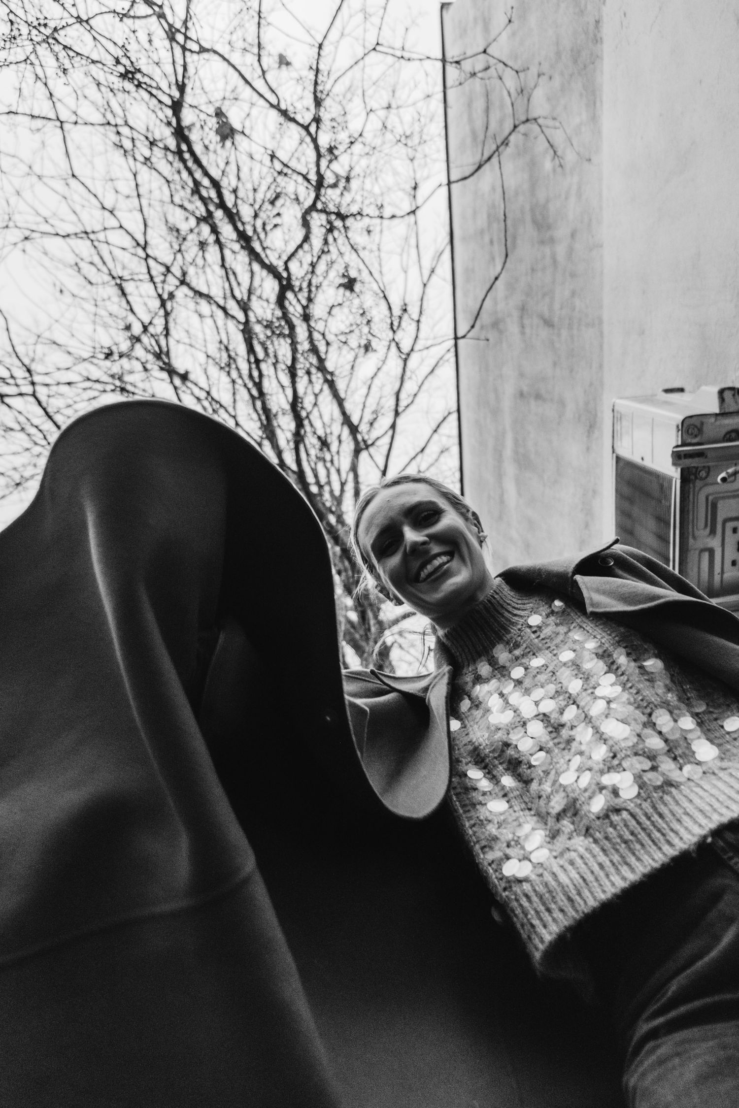 Black and white photo of someone laughing joyfully while wearing a patterned sweater outdoors.