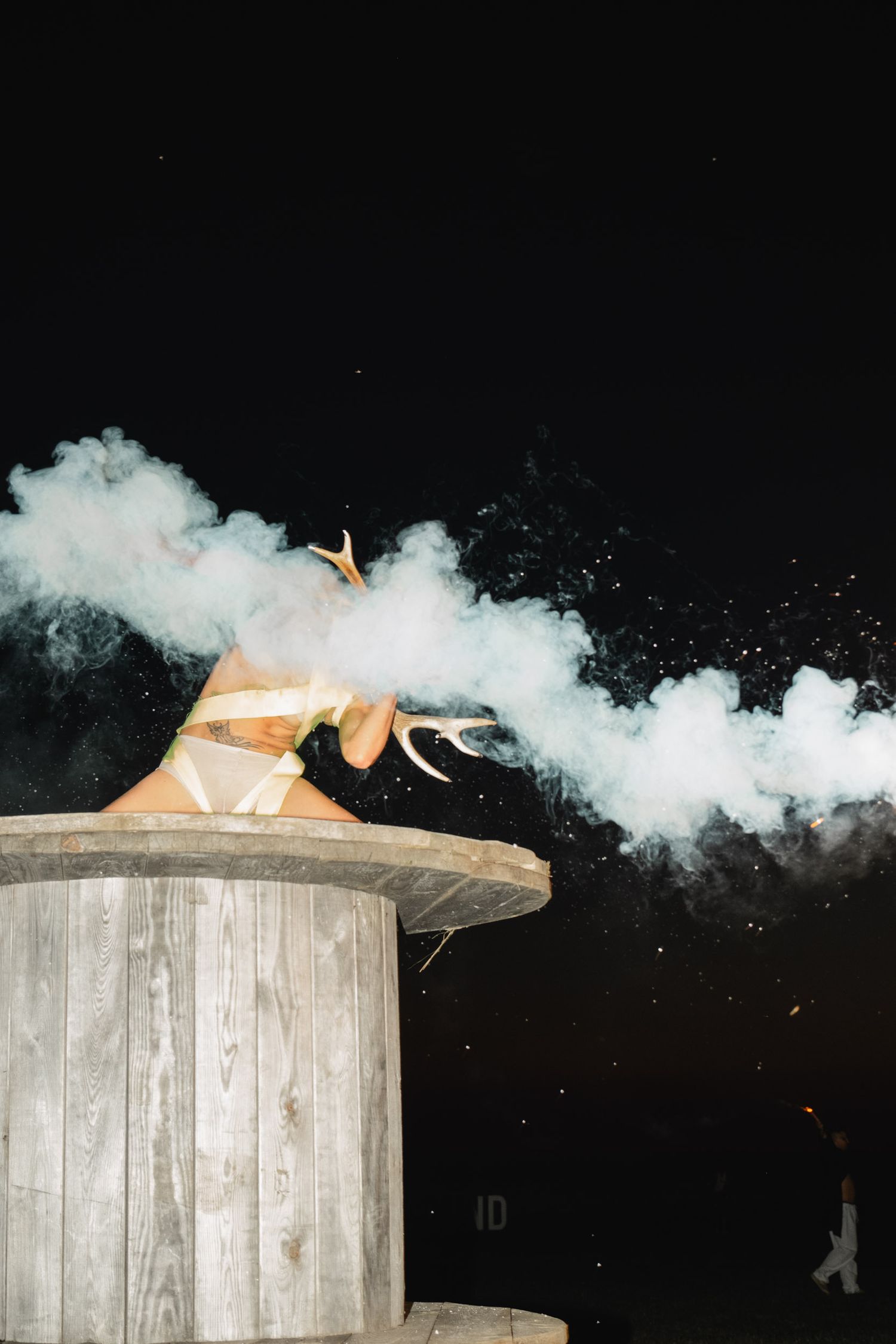 Dramatic smoke effect around a figure on a circular platform at night.