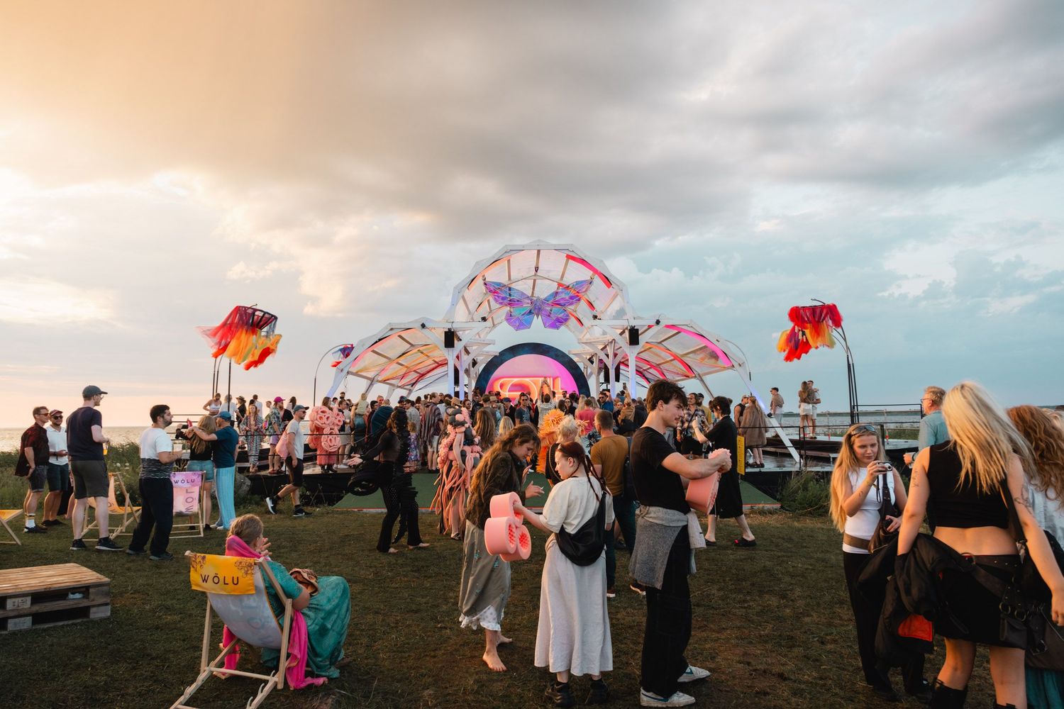 Colorful festival scene with people gathering under sunset sky.