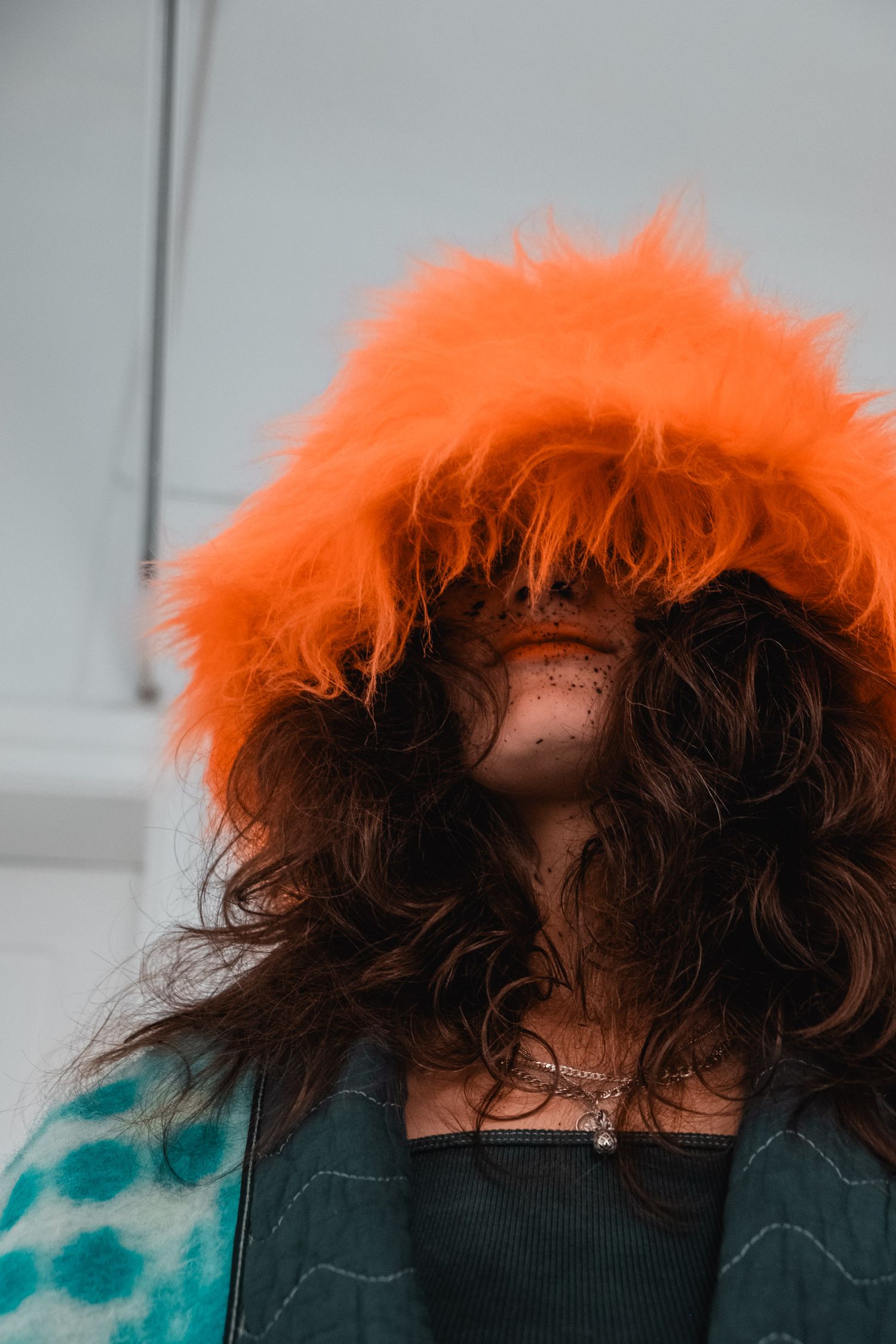 Person wearing bright orange fur-trimmed hood against white wall.
