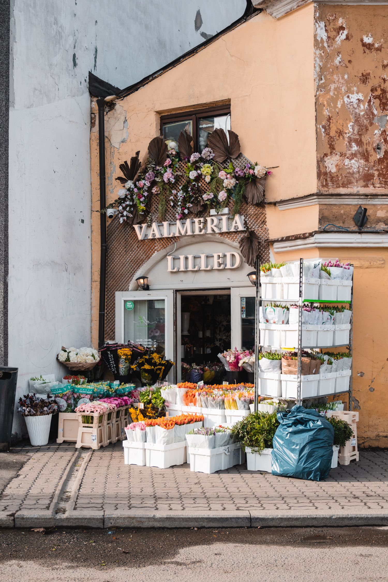 Charming flower shop storefront with Valmeria Lilled sign and buckets of fresh flowers displayed outside.